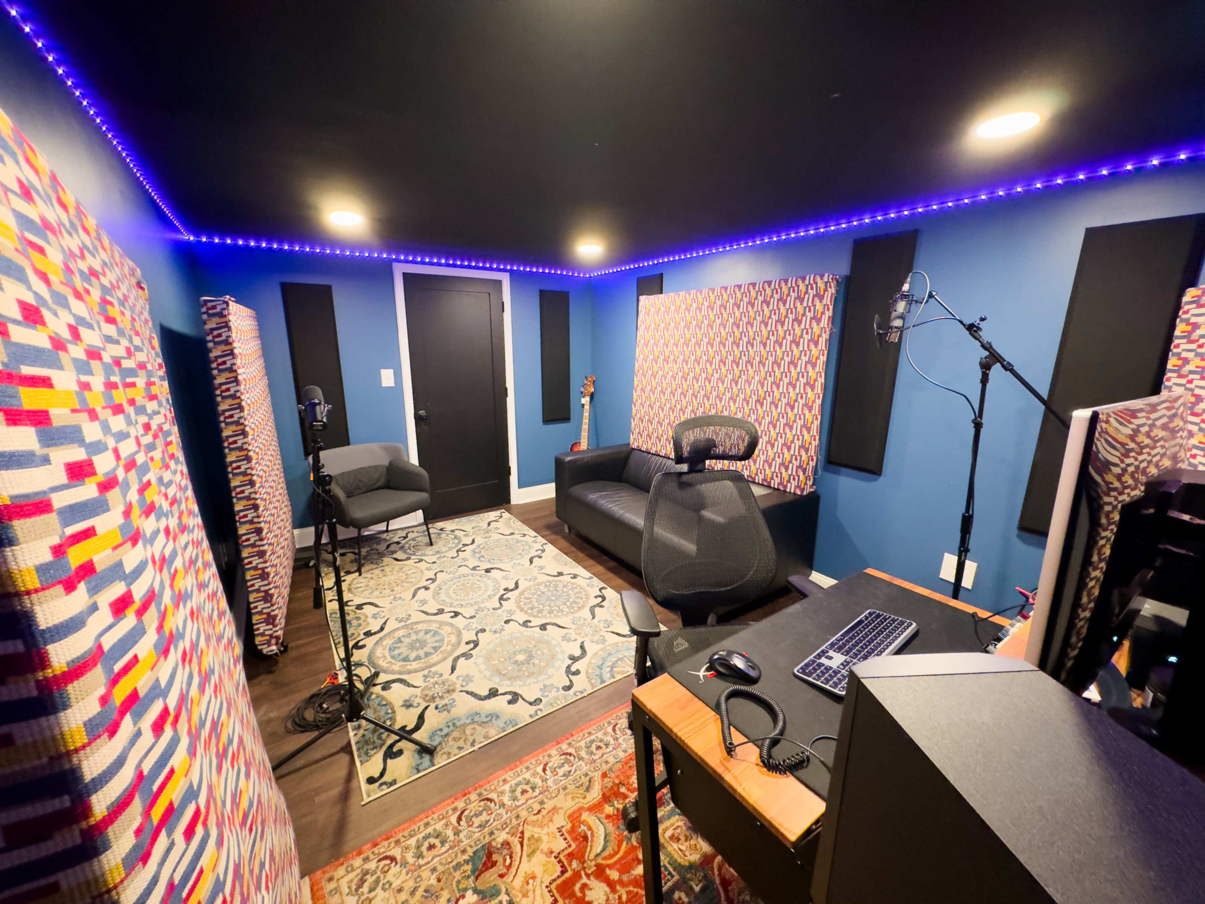 A soundproof recording studio featuring a couch, microphone stands, acoustic panels on the walls, and a desk with a computer.