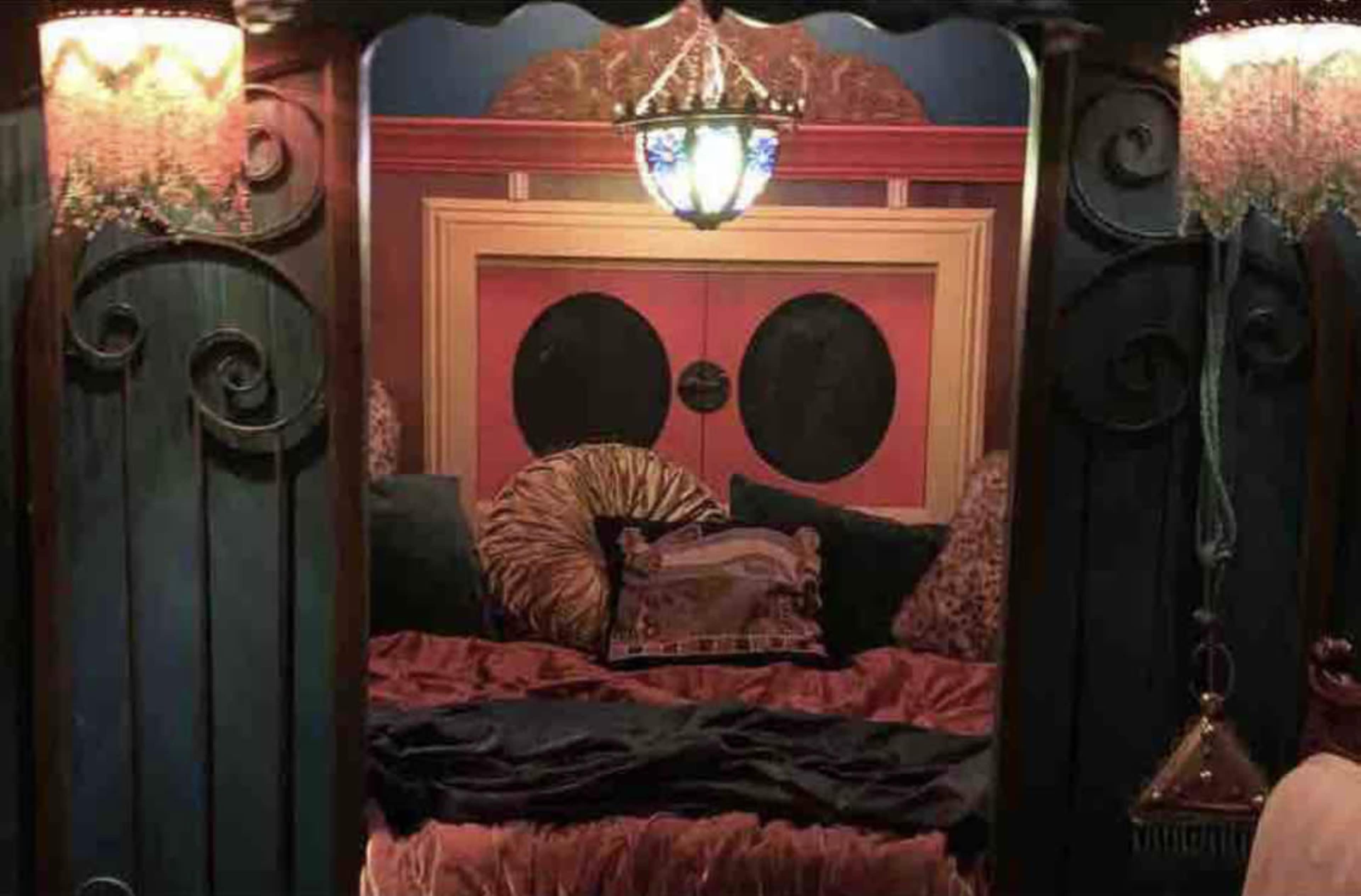 A dimly lit bedroom with a stylized bed featuring decorative pillows and a colorful headboard.