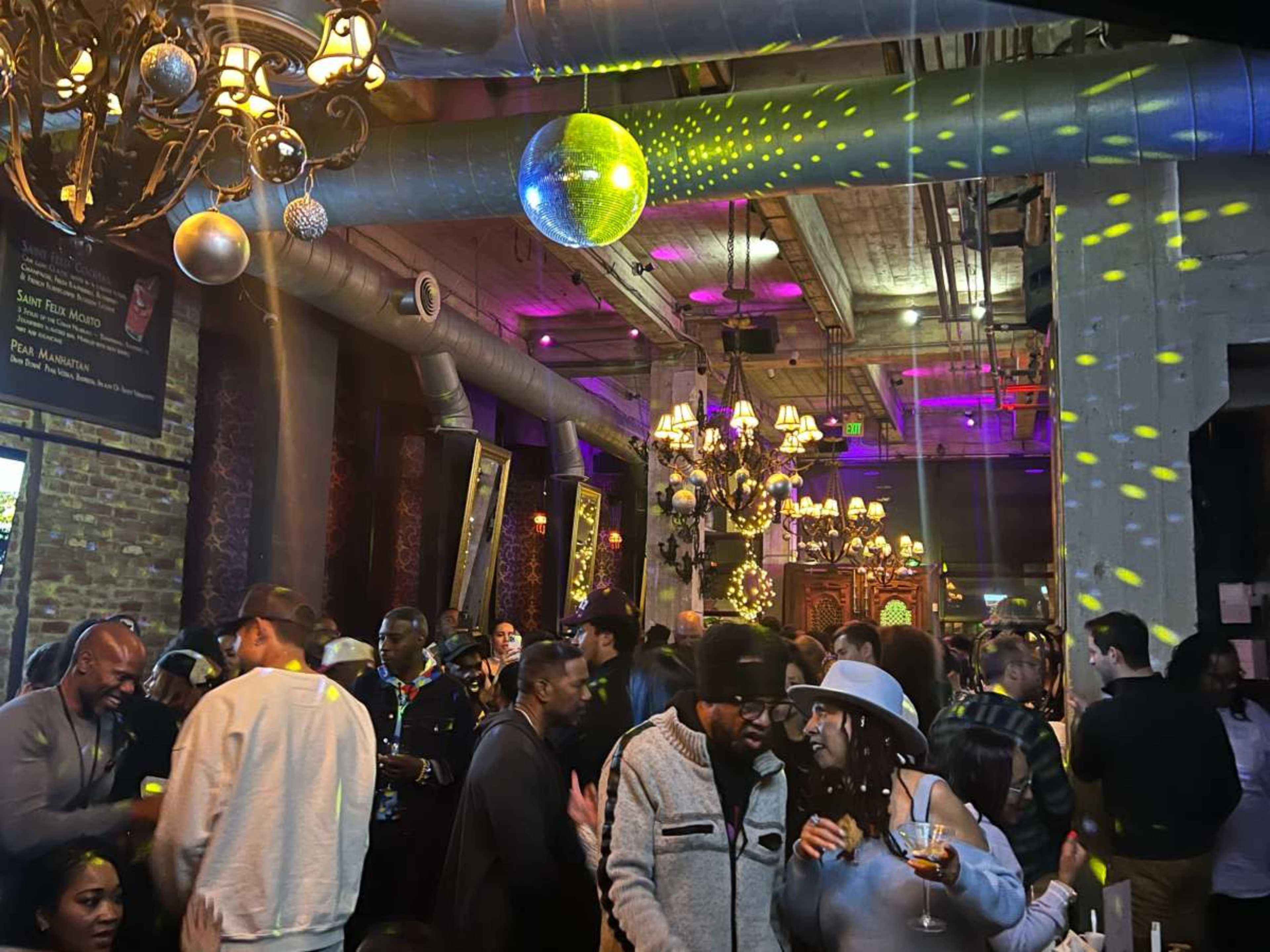 The image shows a lively bar scene with people socializing under colorful lights and disco balls.