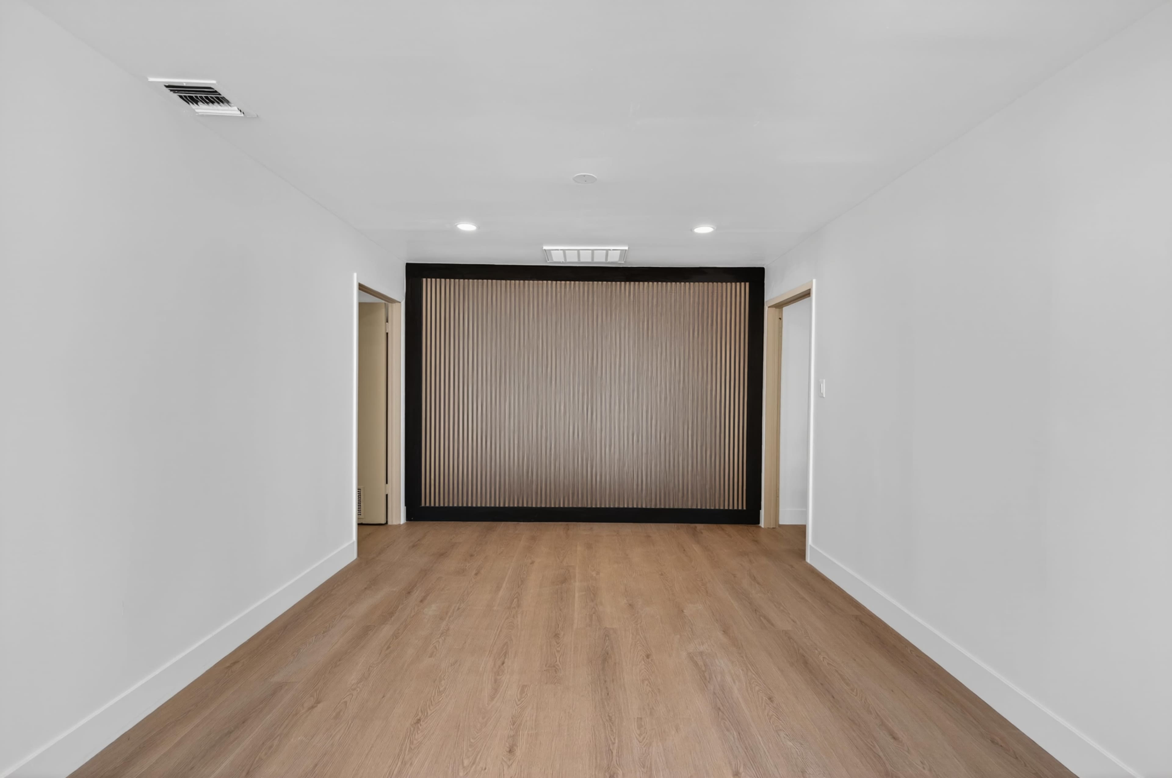 The image shows a spacious room with light wood flooring and a central decorative wall featuring vertical slats, flanked by open doorways.