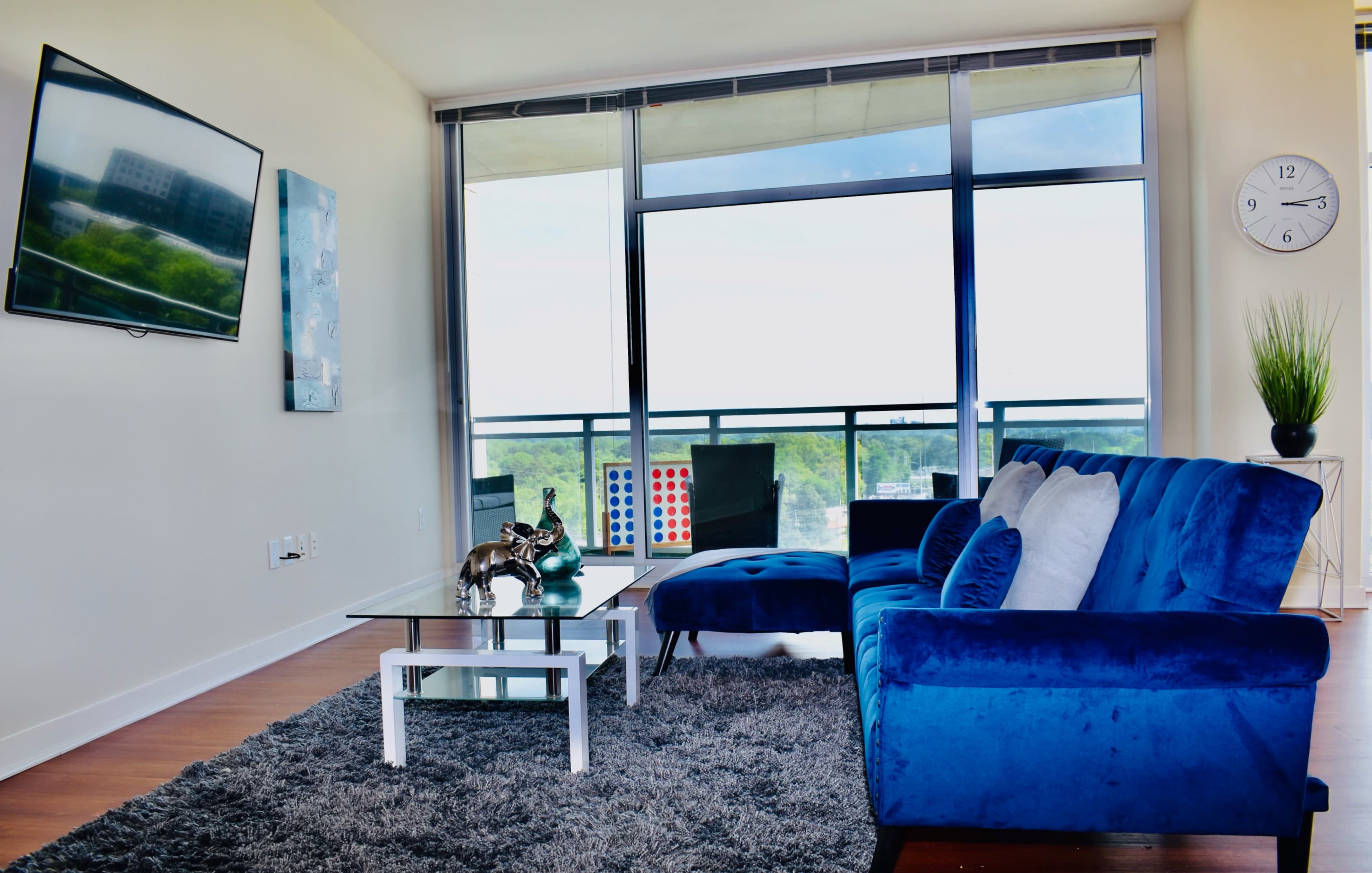 A modern living room features a blue sofa, coffee table, and a large window with a view.