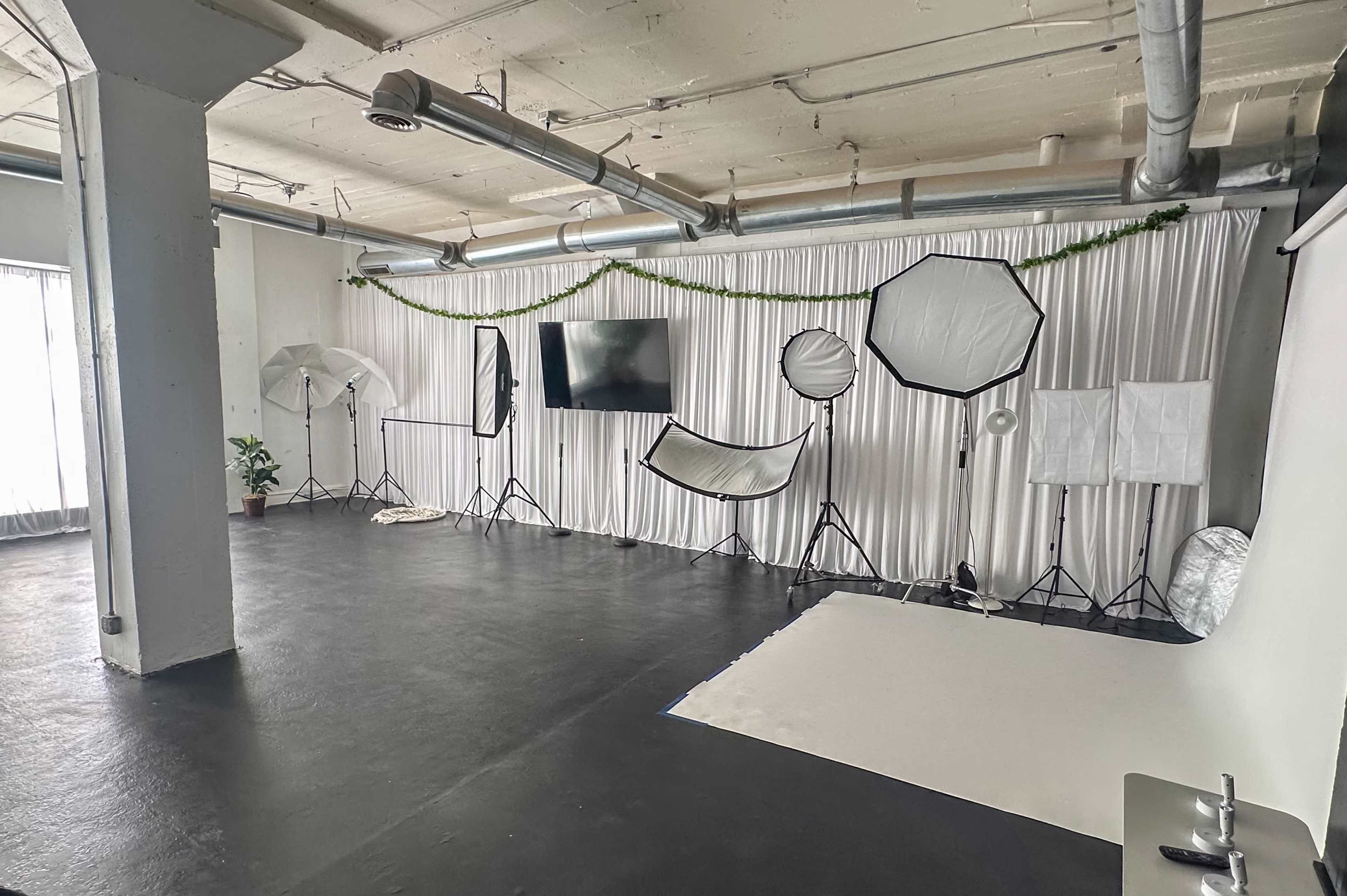 The image shows a photography studio equipped with various lighting equipment and backdrops against a white curtain.