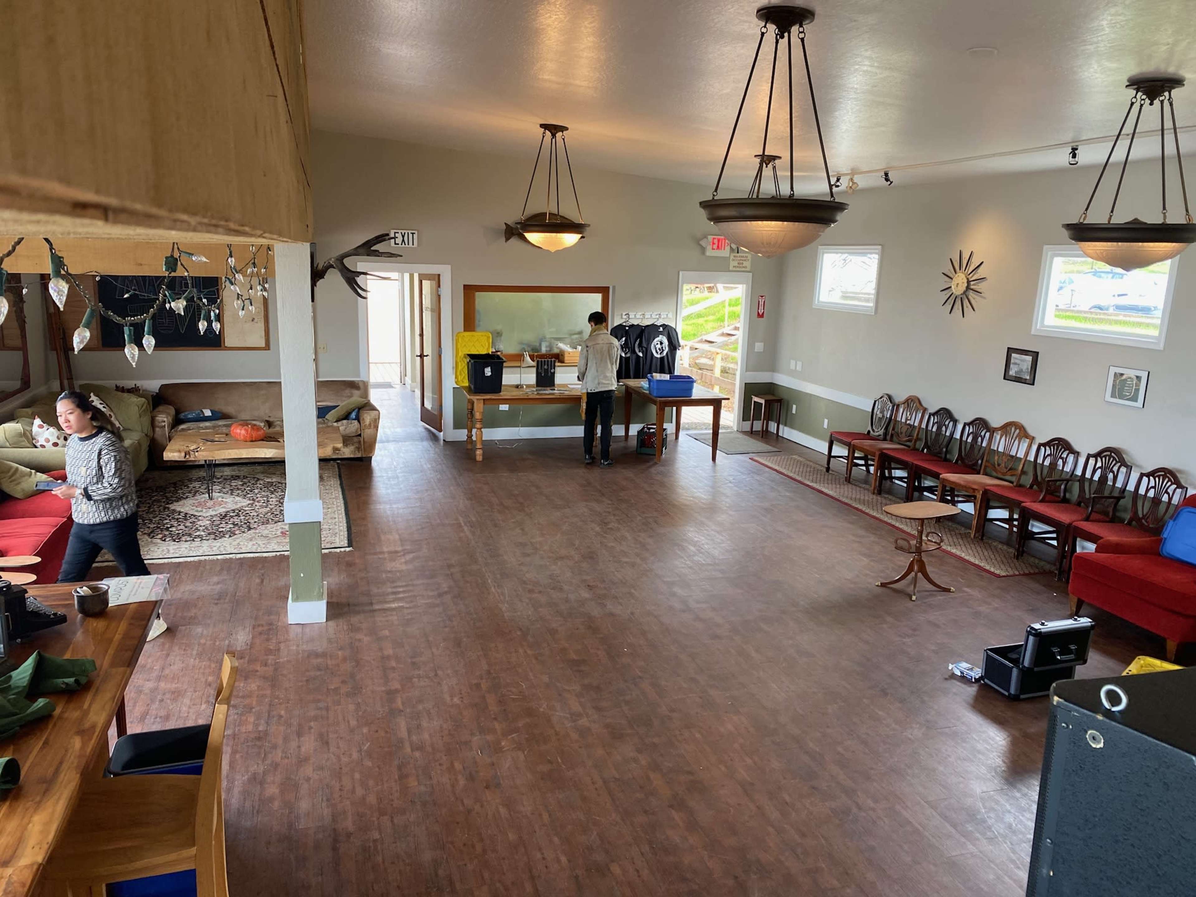 The interior of a spacious community room features a seating area with sofas, a serving counter, and a few people engaging in activities.