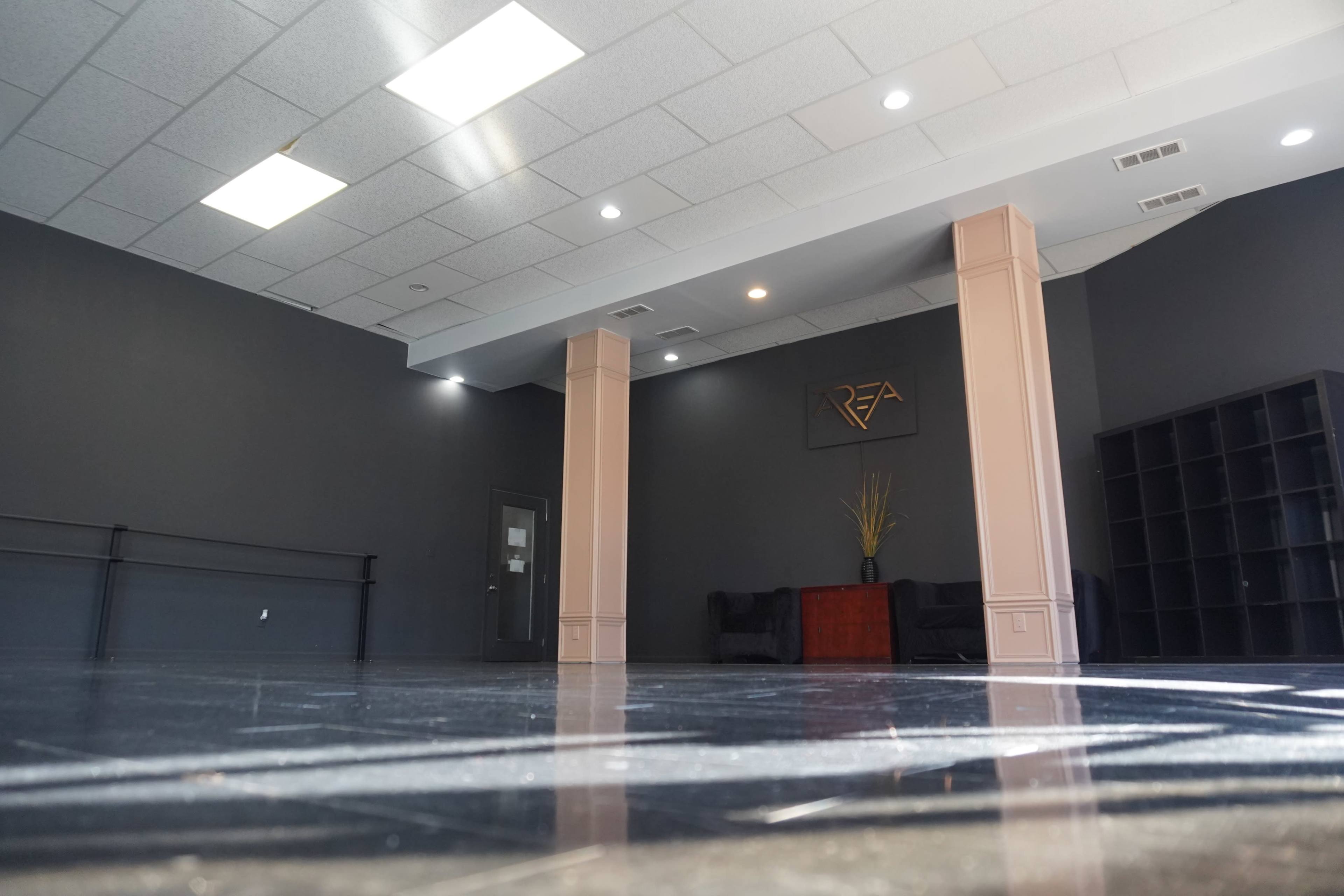 An empty room with dark gray walls, polished flooring, and two light-colored columns, featuring a seating area and a wall shelf.