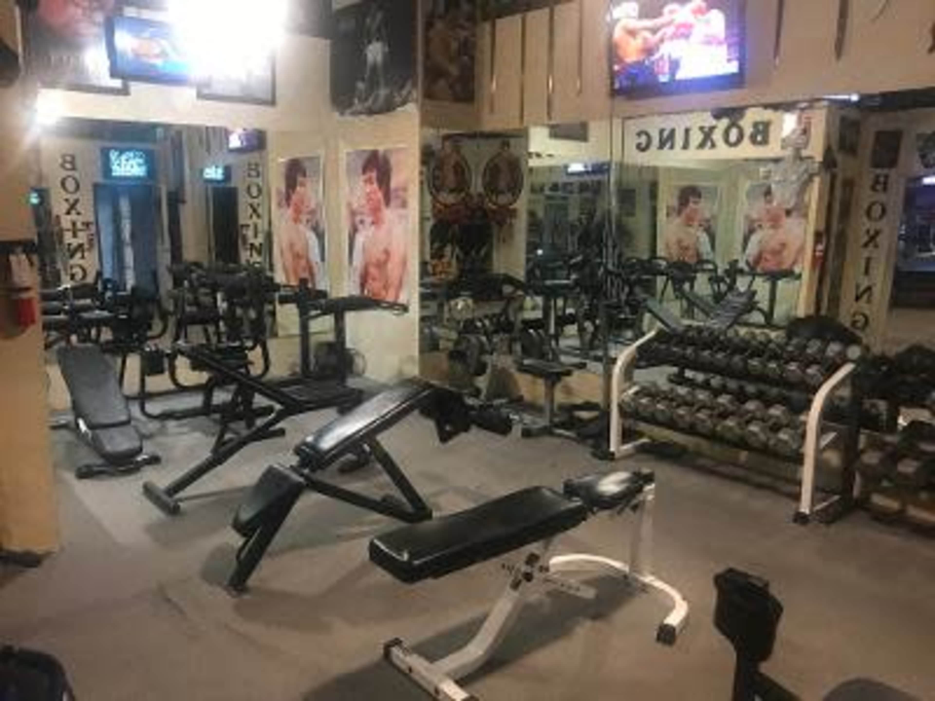 The image shows a boxing gym with various workout equipment, including weights, benches, and a television displaying a boxing match.