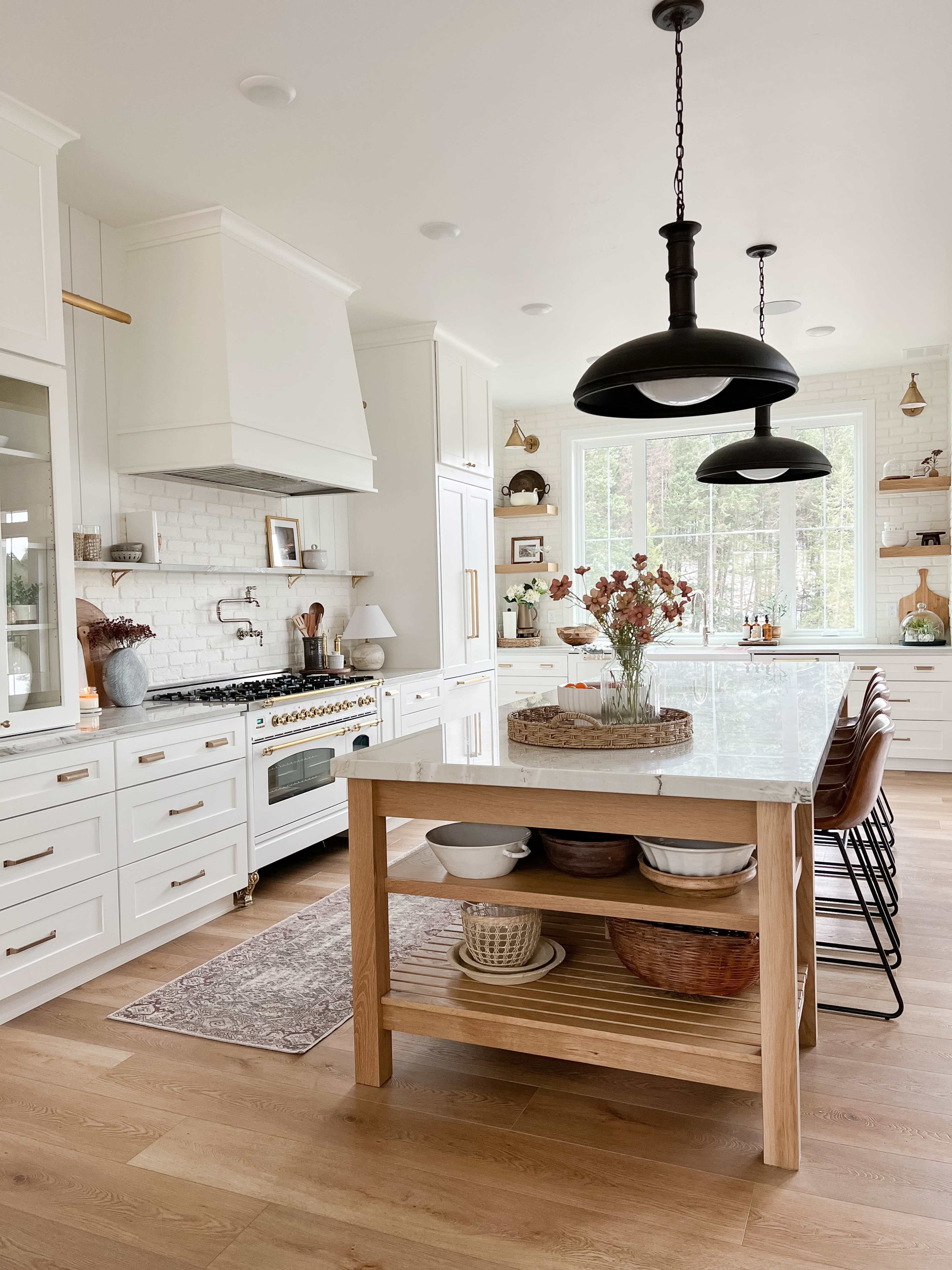 The kitchen features white cabinetry, a large island with a light wood base and open shelving, and black pendant lights hanging above the countertop.