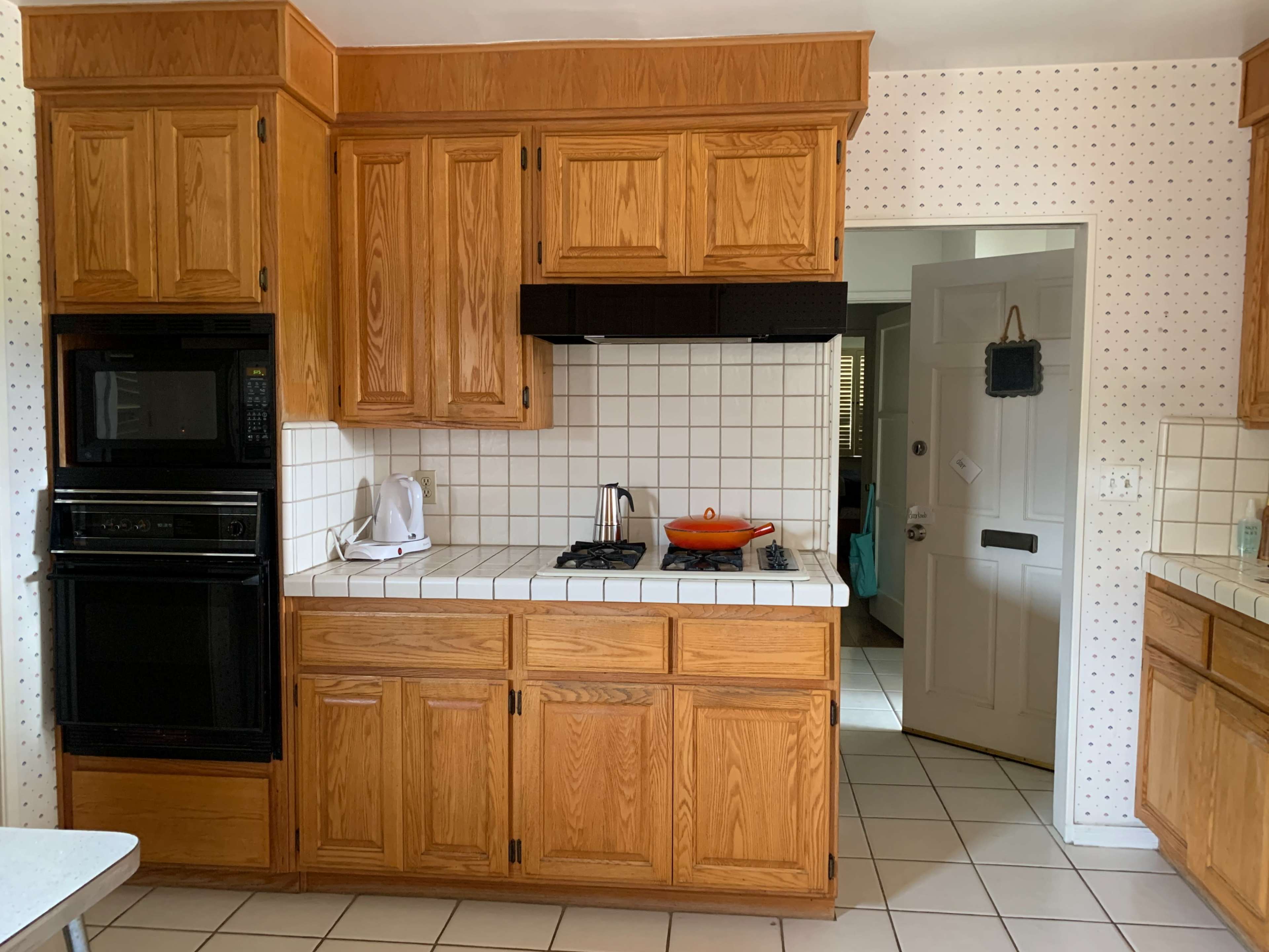 A kitchen with wooden cabinets, a tiled countertop, a stovetop, and a door leading to another room.