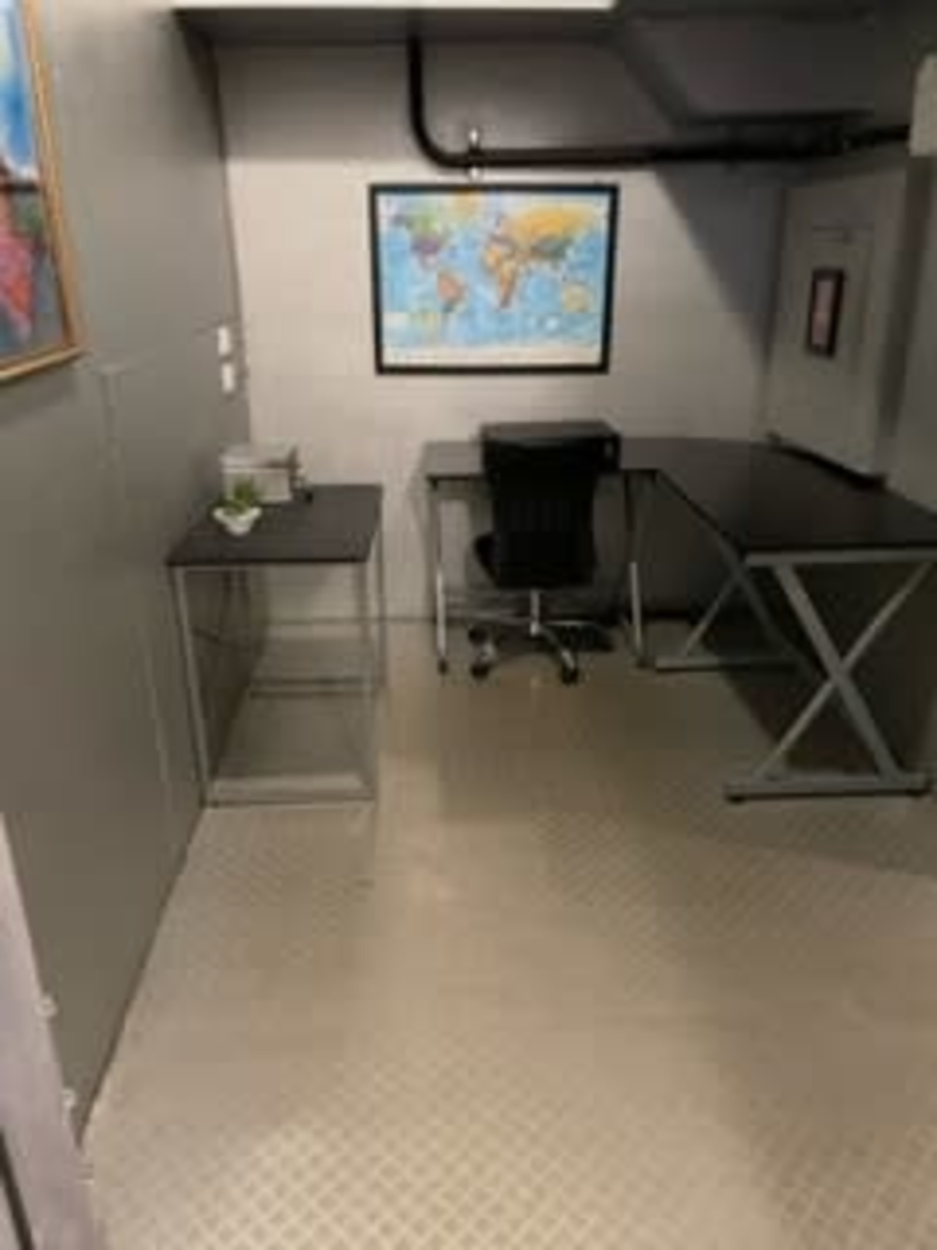 A small, sparse office space featuring a desk with a chair, a glass side table, a world map on the wall, and minimal decor.