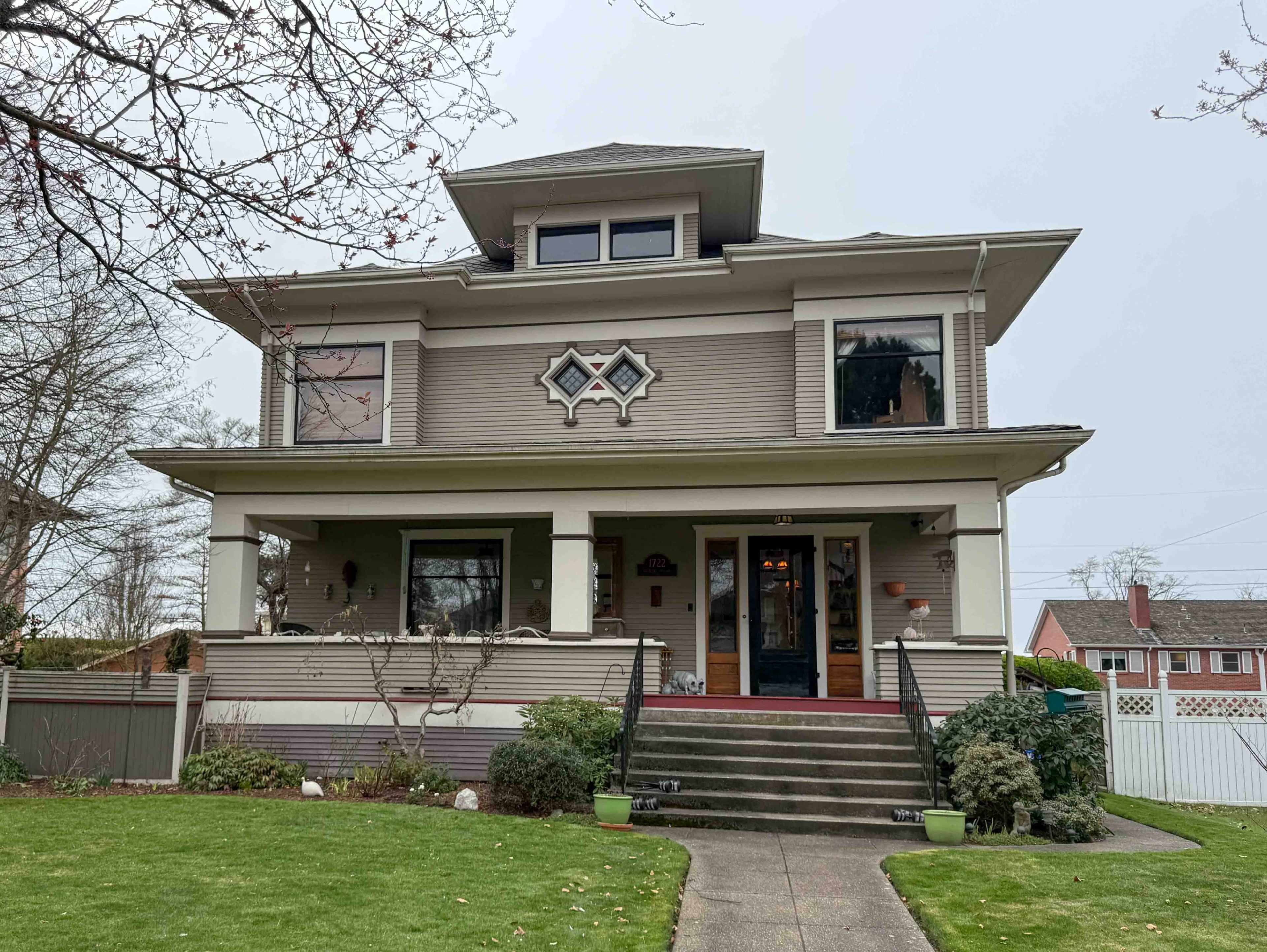The image shows a large, two-story house with a detailed facade, featuring a front porch, multiple windows, and a landscaped yard.