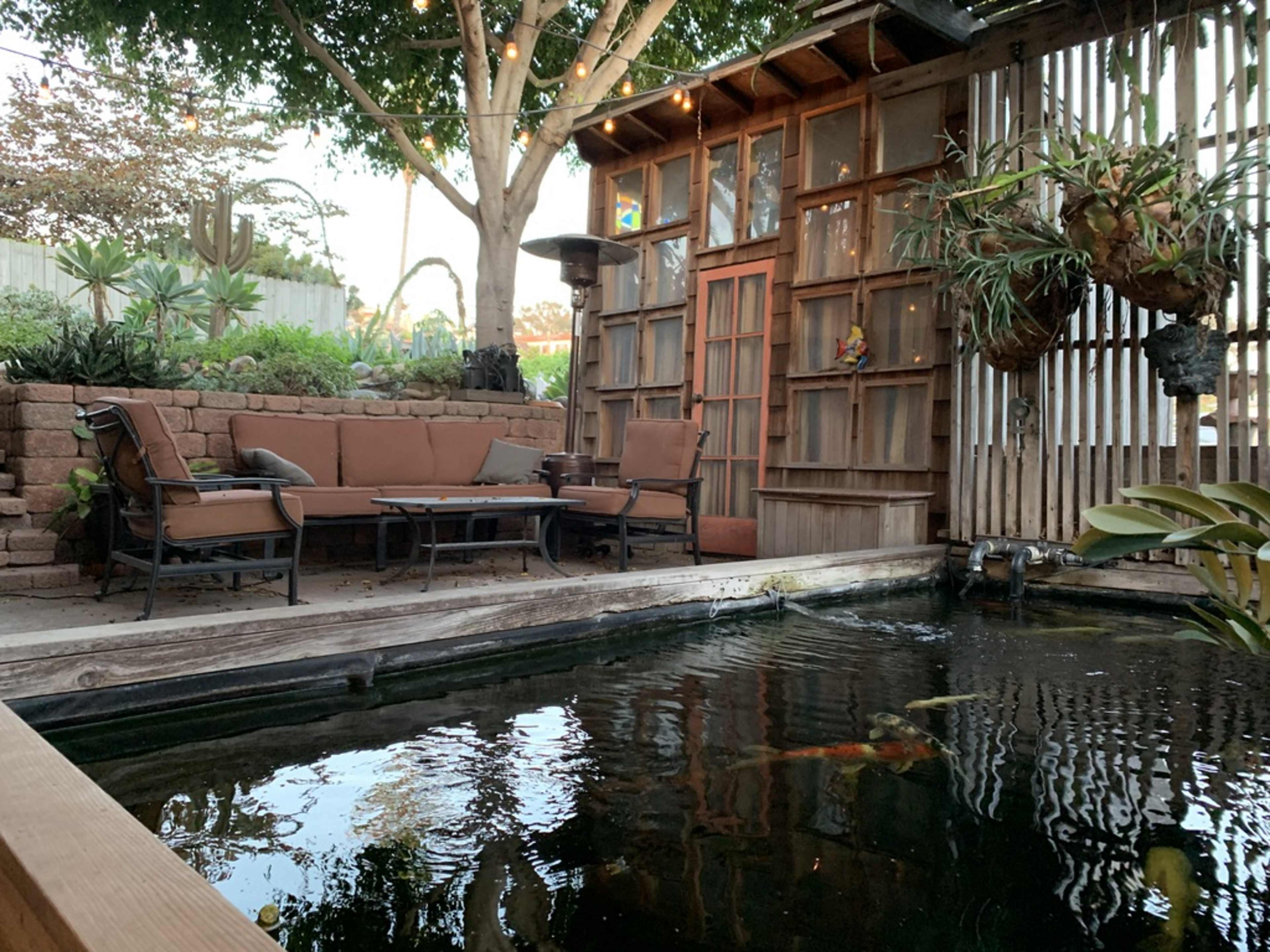 A cozy outdoor seating area beside a koi pond, surrounded by plants and wooden structures.