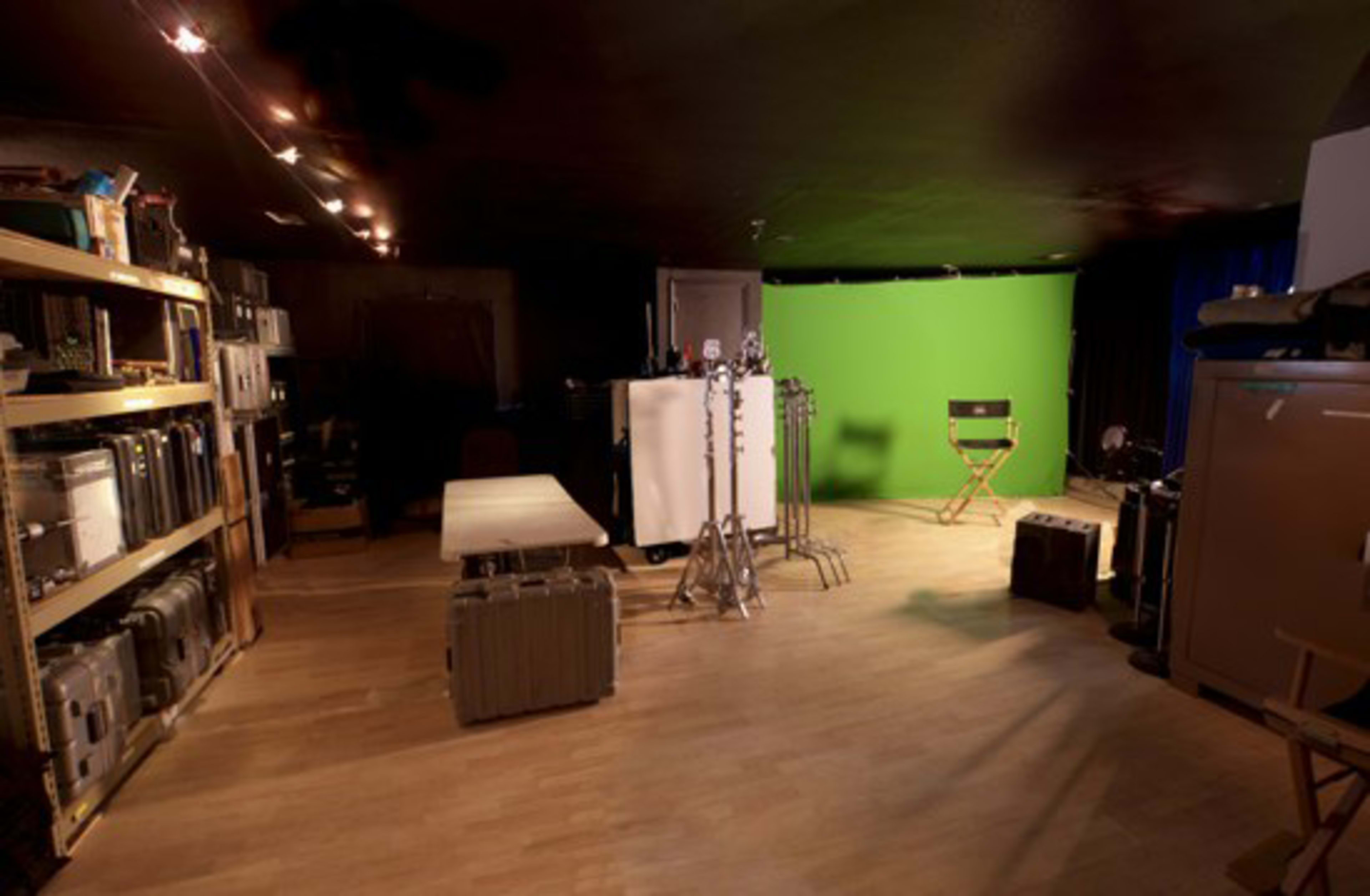 A room with storage shelves filled with equipment cases, a green screen setup, and a director's chair.