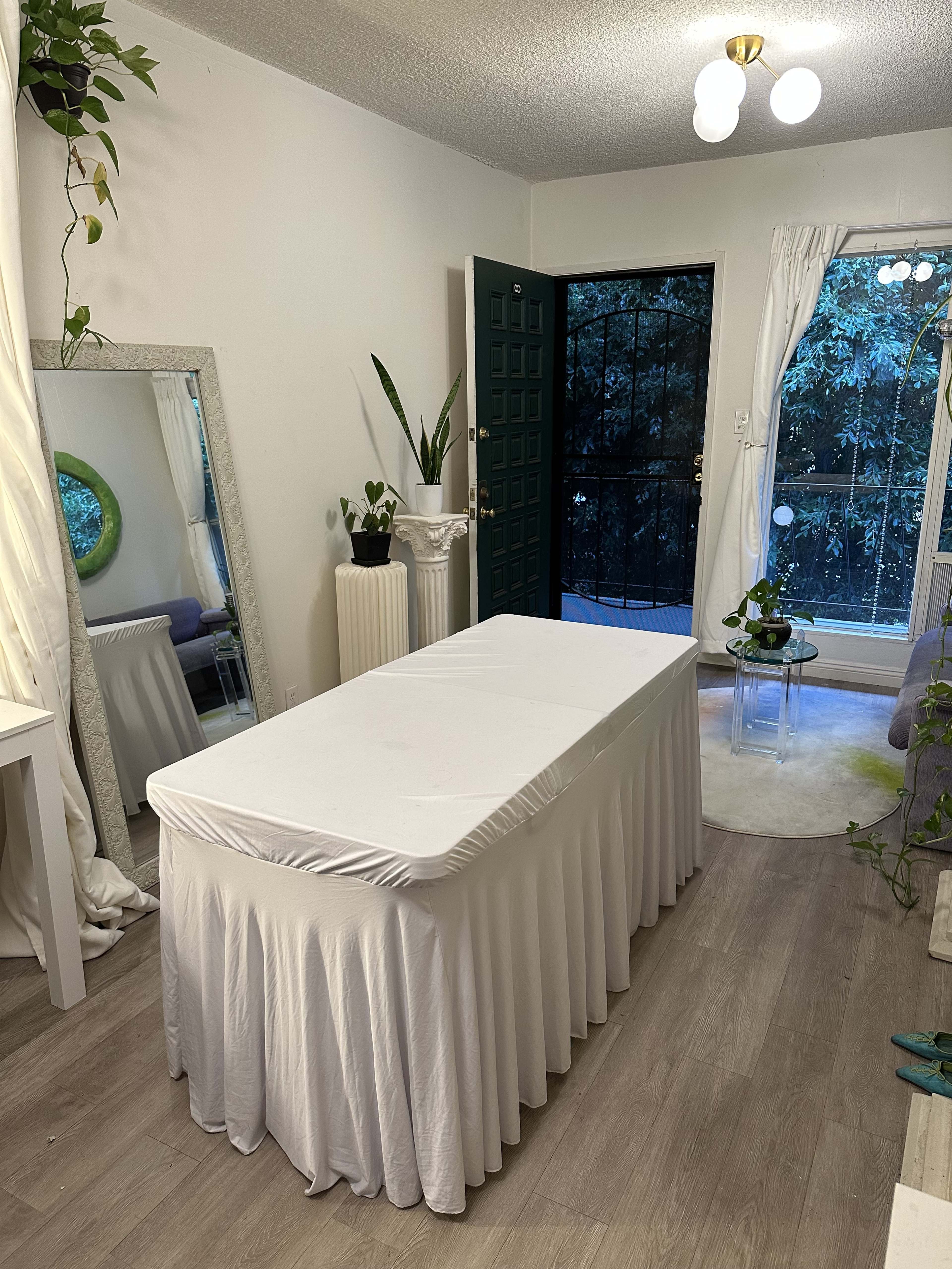 A white table covered with a tablecloth is positioned in a well-lit room near an open door that leads to a patio.