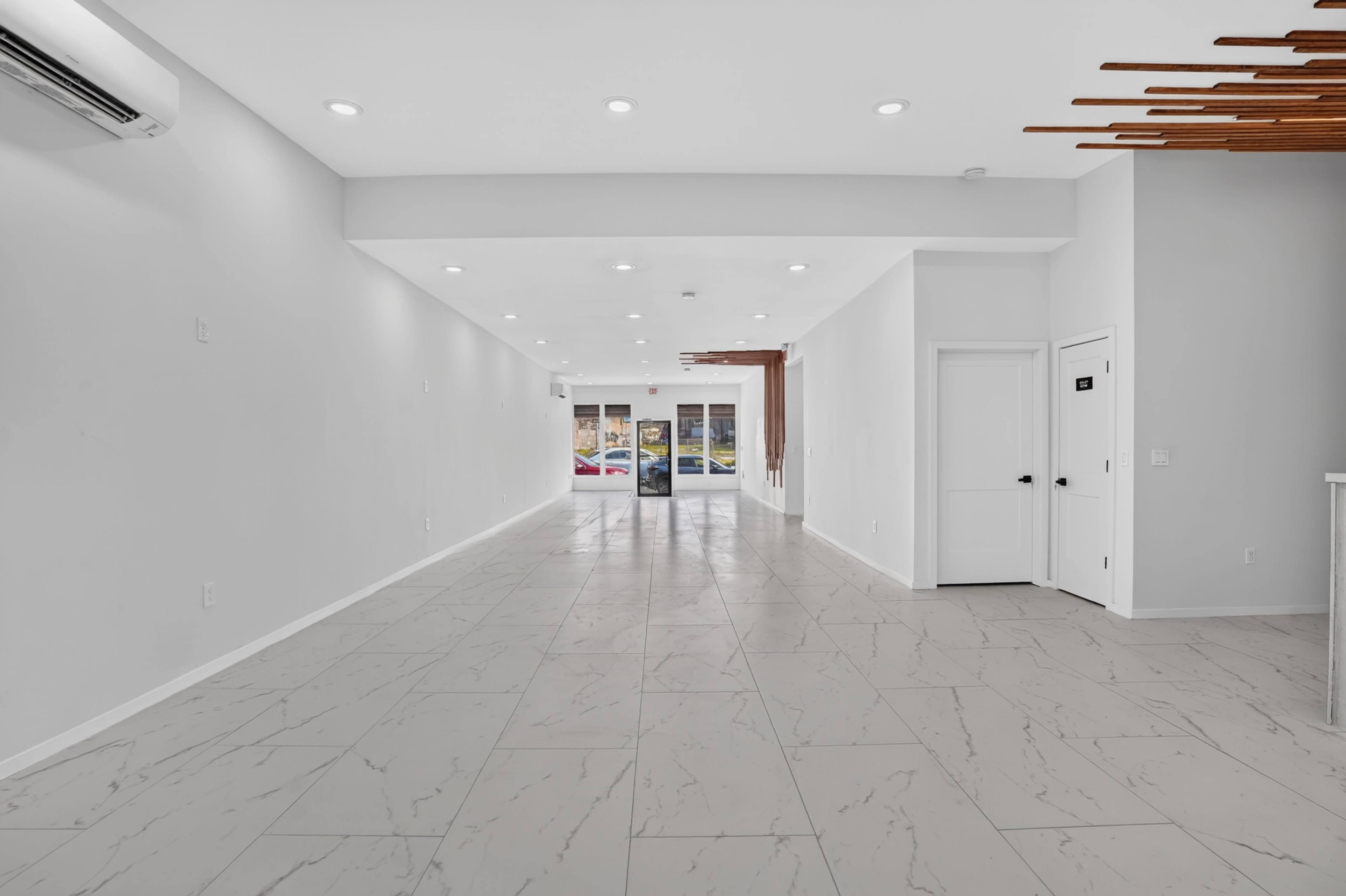 The image shows a spacious, modern interior of a commercial space with white walls, tile flooring, and large windows at the entrance.