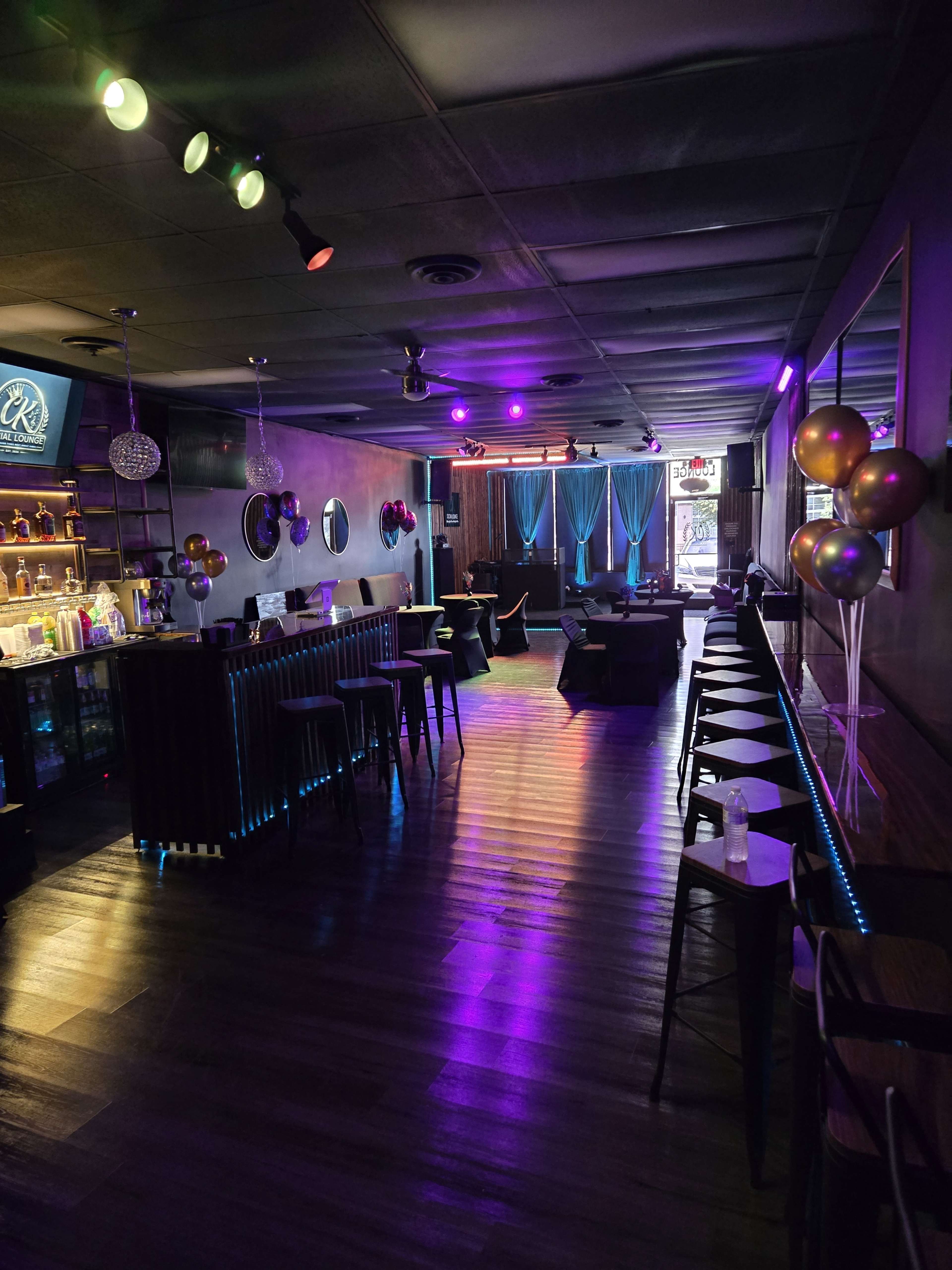 The image shows a dimly lit bar/lounge area with colorful lighting, empty chairs, and decorative balloons.