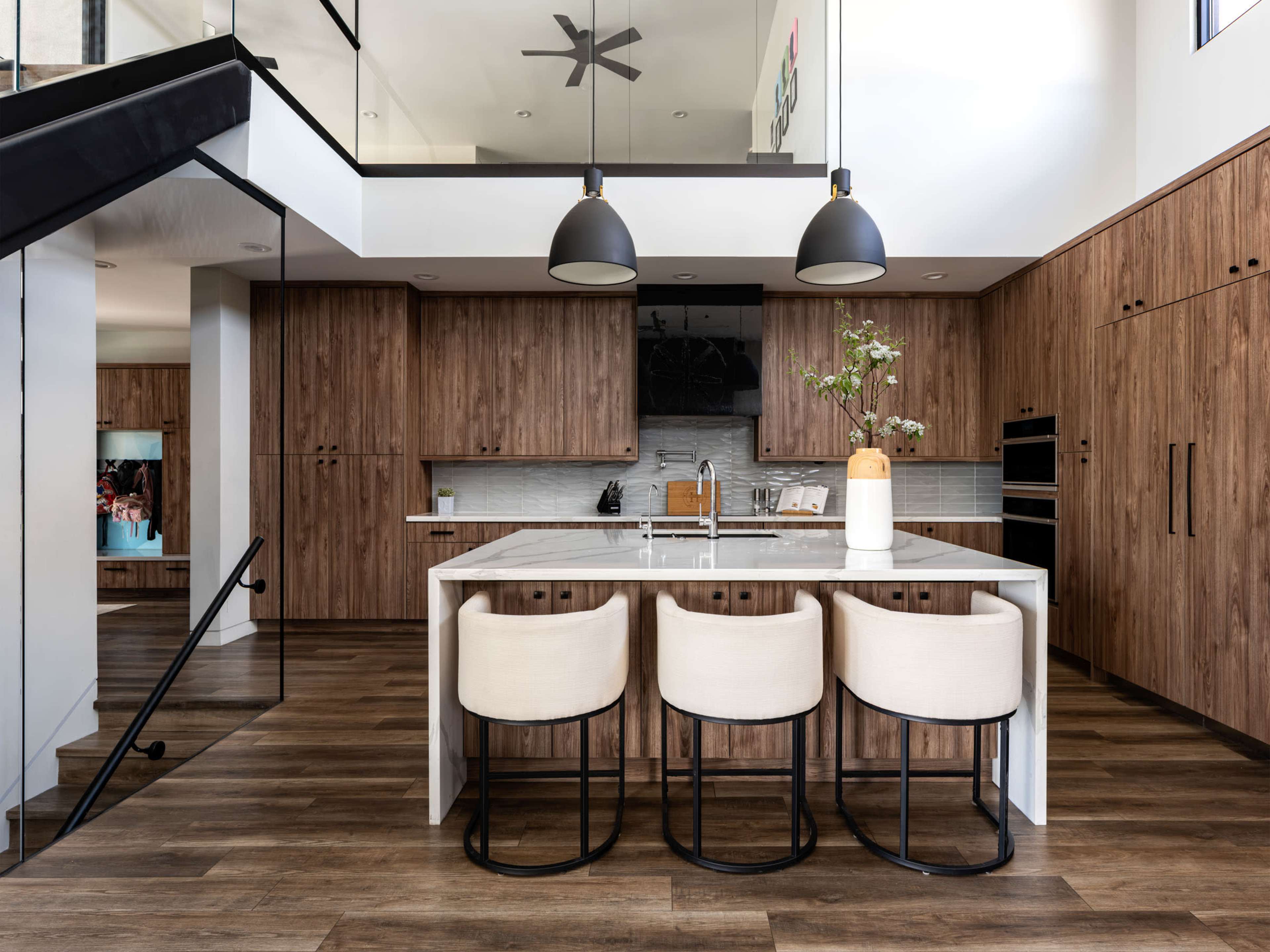 The modern kitchen features wooden cabinetry, a central island with three bar stools, and large pendant lights hanging above.