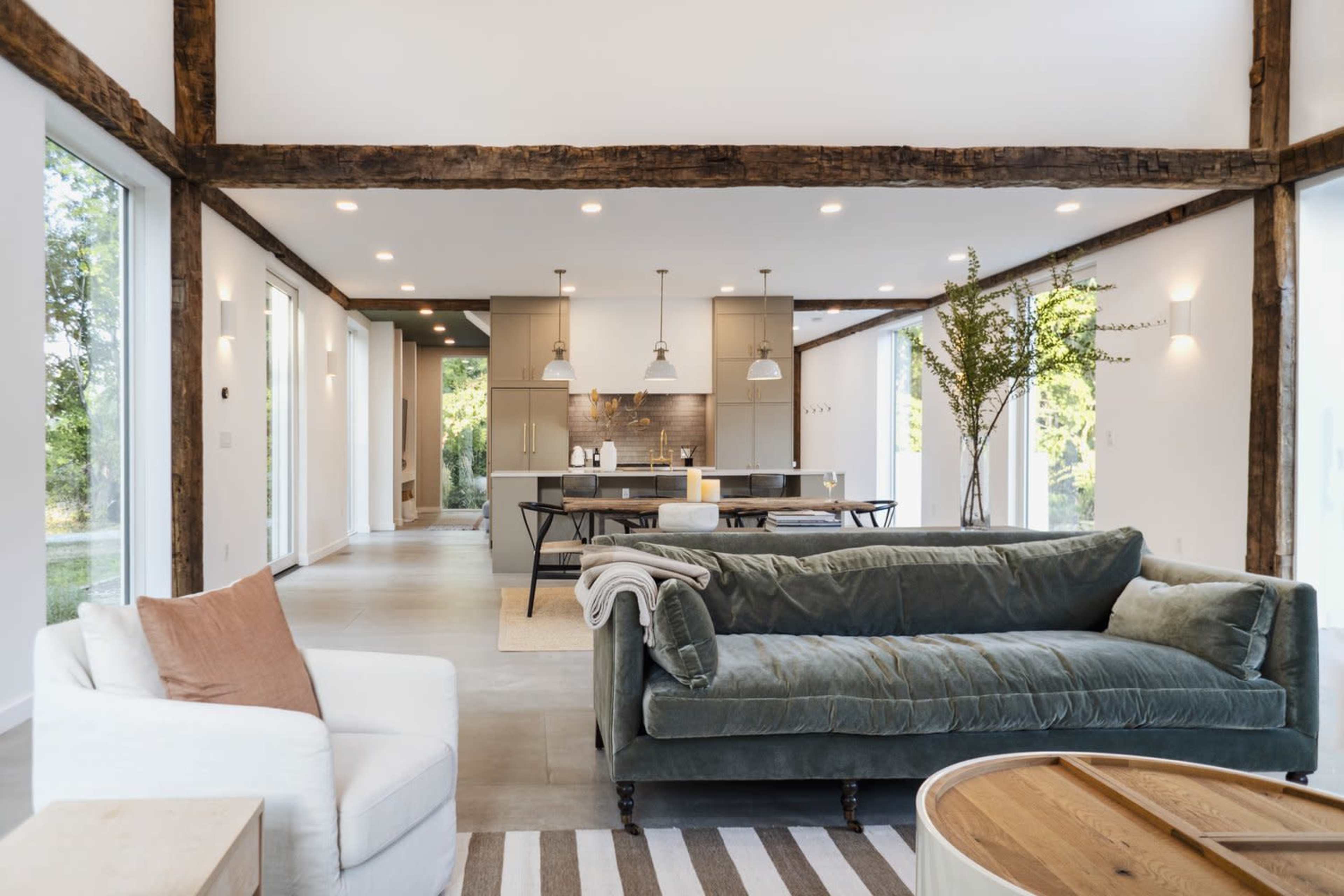 A spacious, modern living area features a green velvet sofa, a white armchair, a wooden dining table, and a well-equipped kitchen in an open layout.