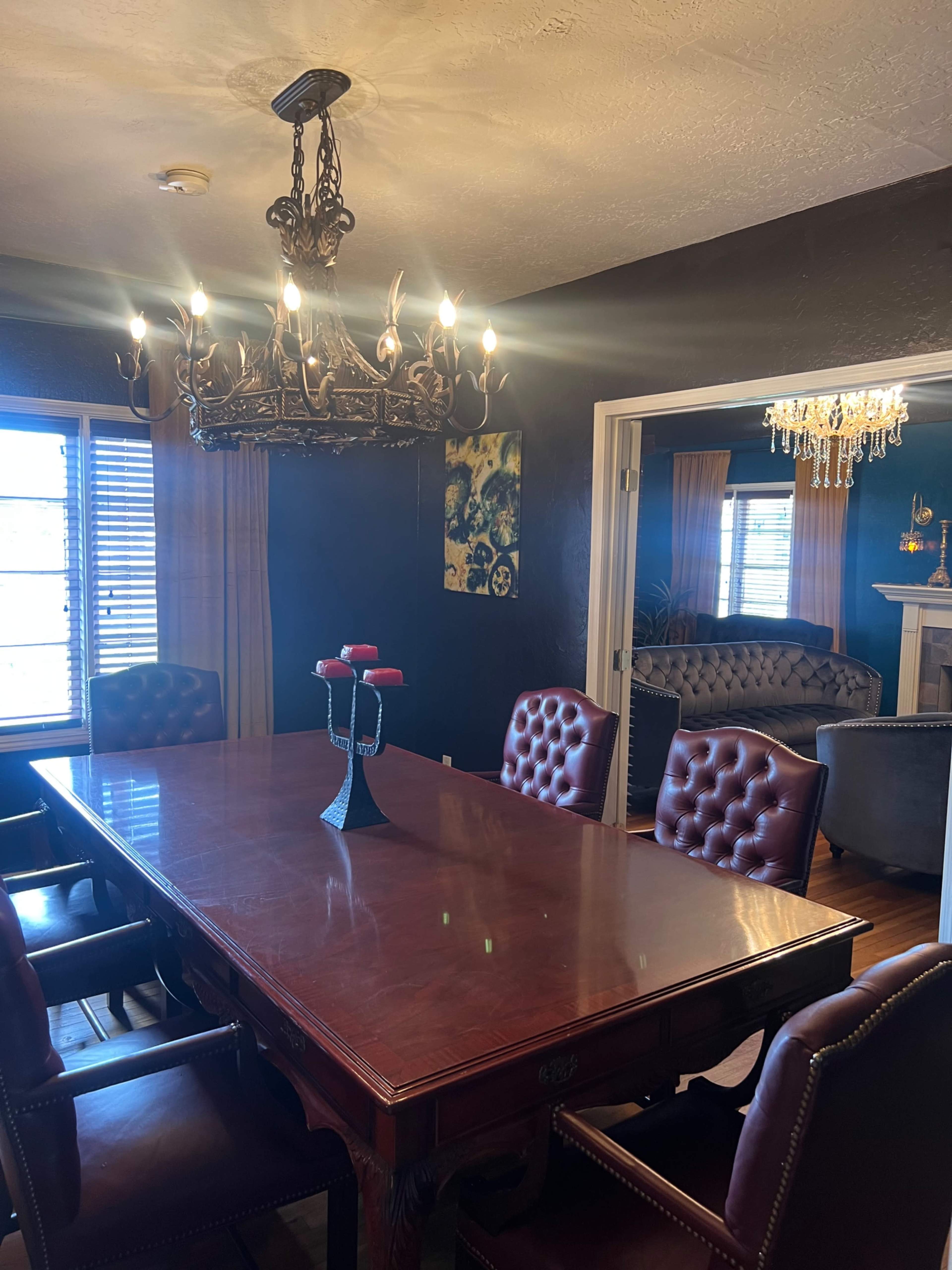 A wooden dining table surrounded by upholstered chairs is illuminated by a chandelier featuring antler designs.
