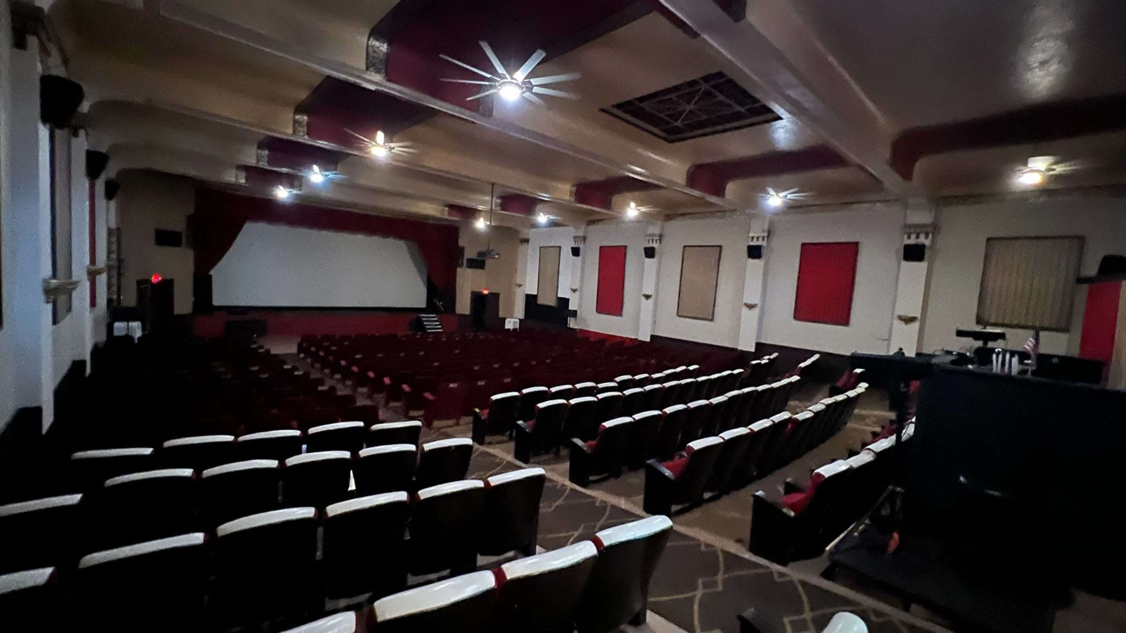 The image shows an empty vintage movie theater with red curtains, multiple rows of seats, and a large screen at the front.