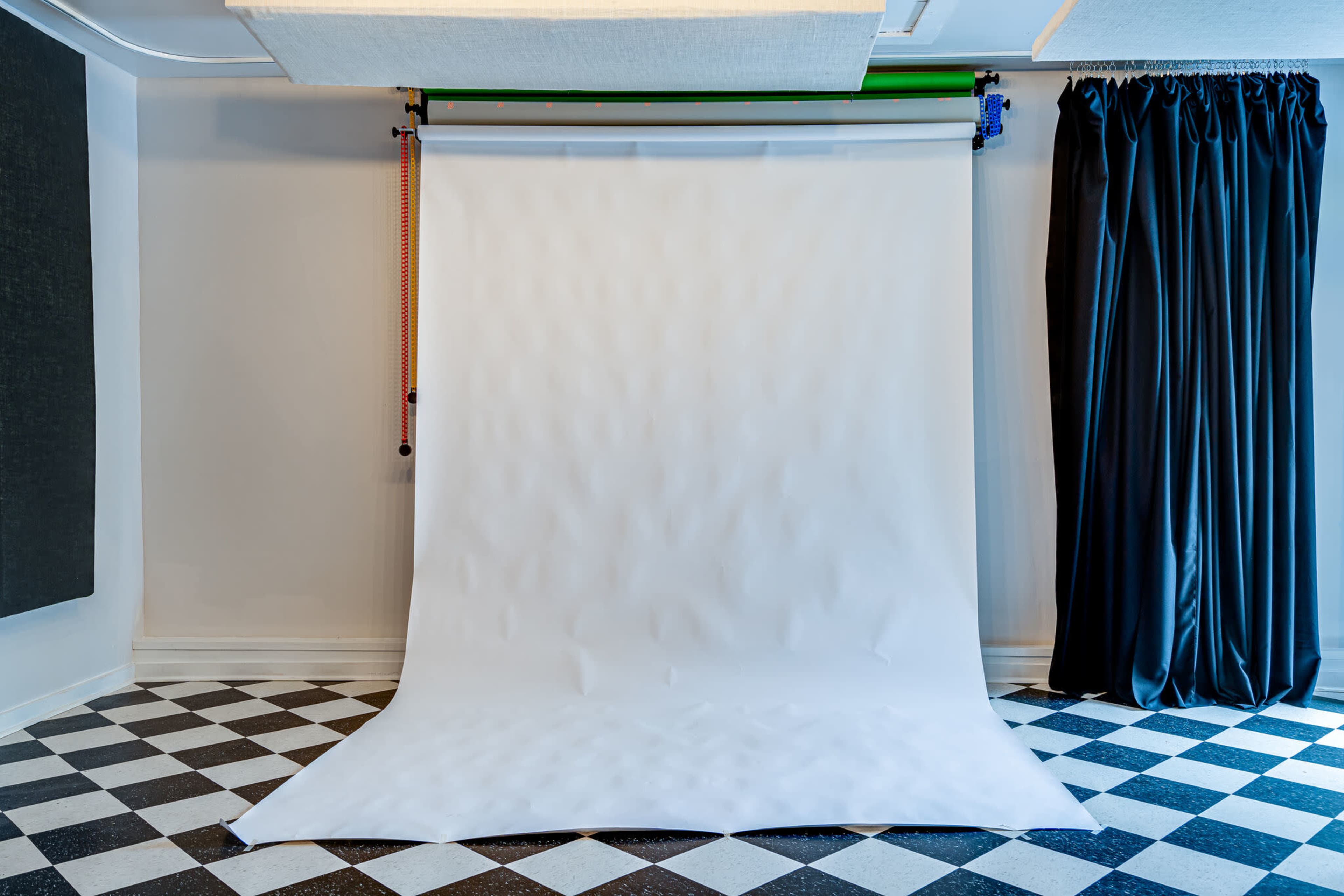 A photography studio with a white backdrop, black and white checkered floor, and a curtain on one side.