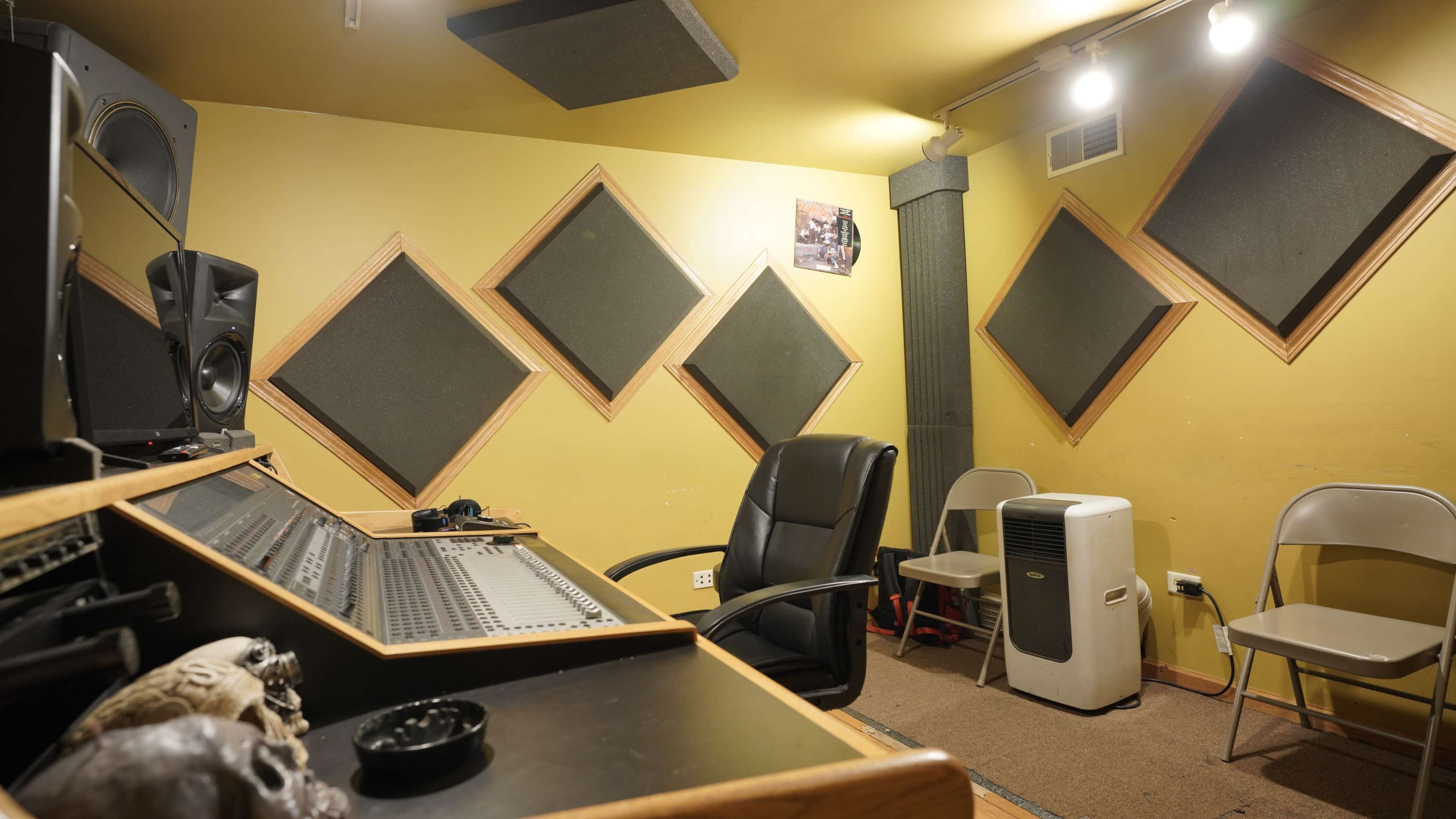 A recording studio with a mixing console, a swivel chair, and audio treatment panels mounted on yellow walls.