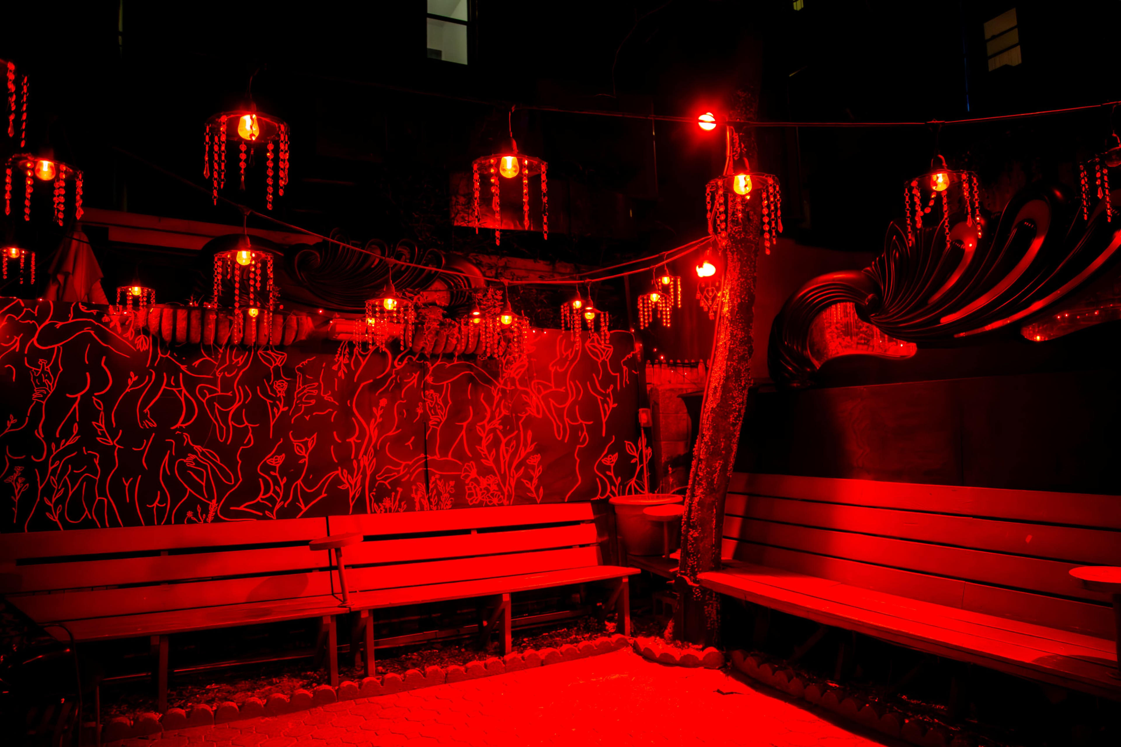 A dimly lit outdoor seating area with red lights and decorative lanterns hanging above wooden benches.