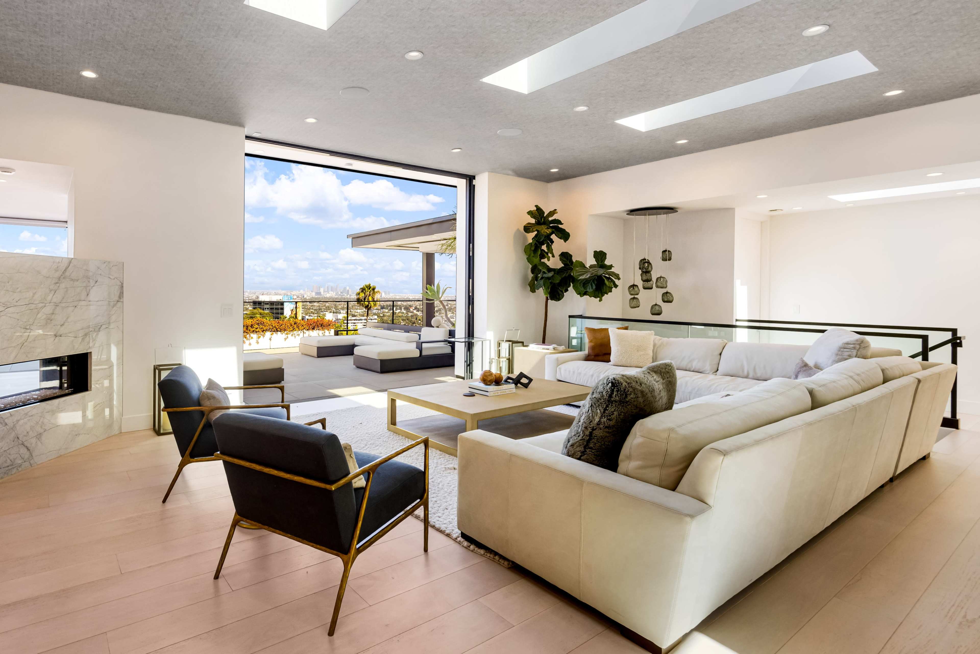 The image shows a modern living room with a large sectional sofa, a coffee table, and a view through sliding glass doors to an outdoor terrace.
