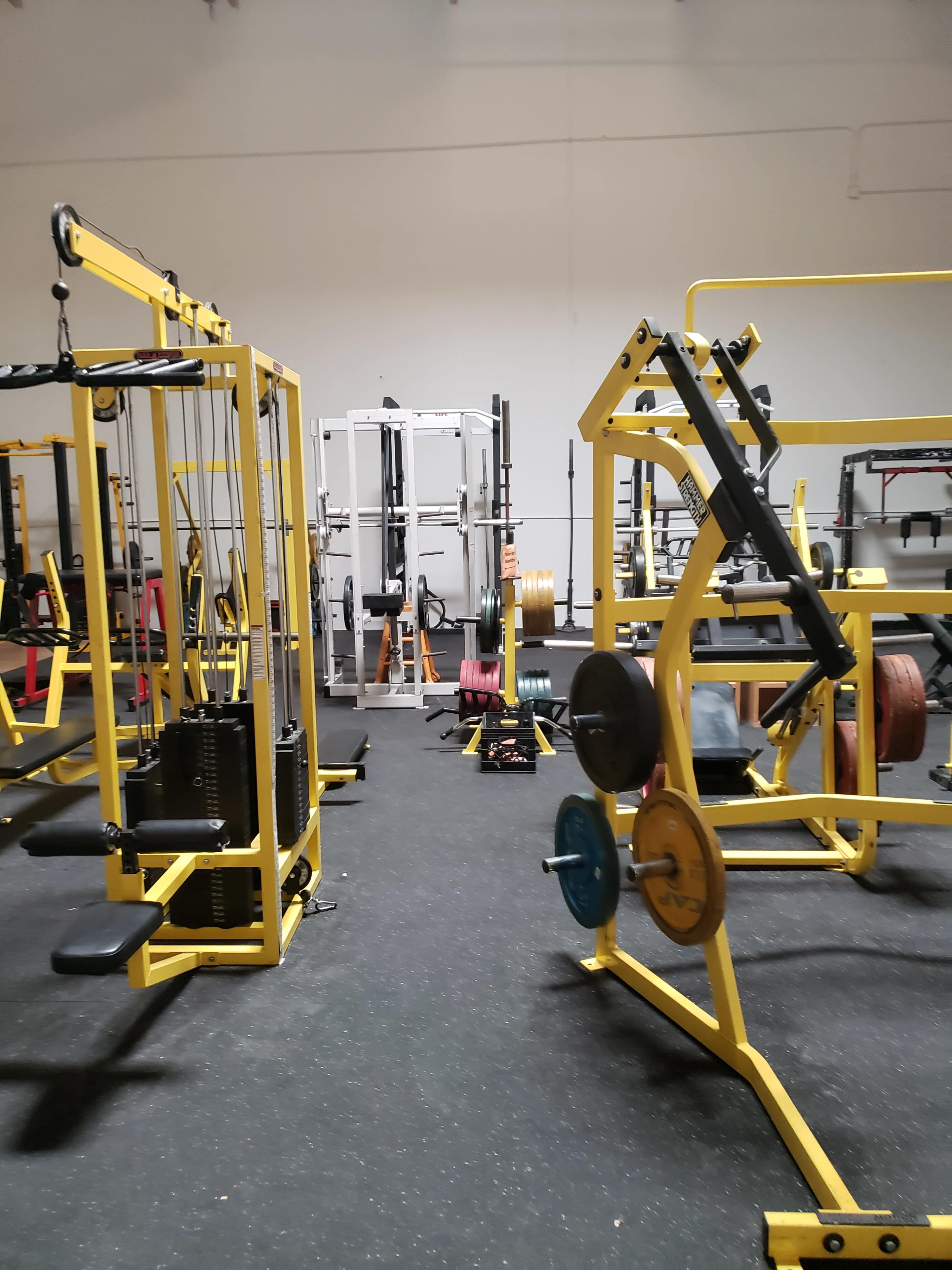 A gym featuring various weightlifting equipment, including a cable machine and a squat rack, all in a spacious workout area.