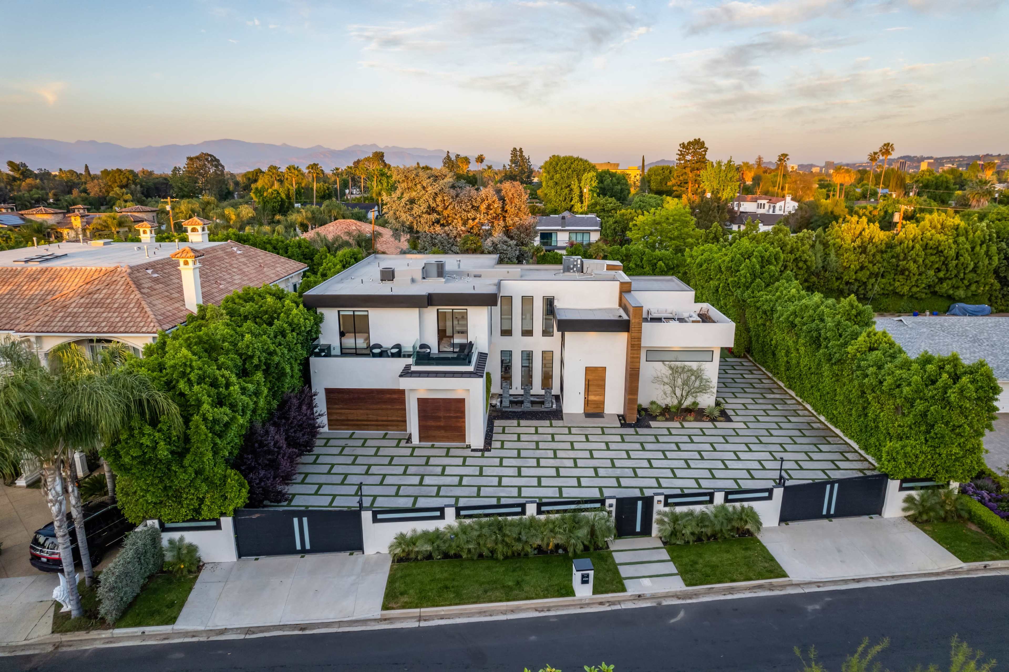 A modern house with a flat roof, surrounded by lush greenery and a stone-paved driveway.
