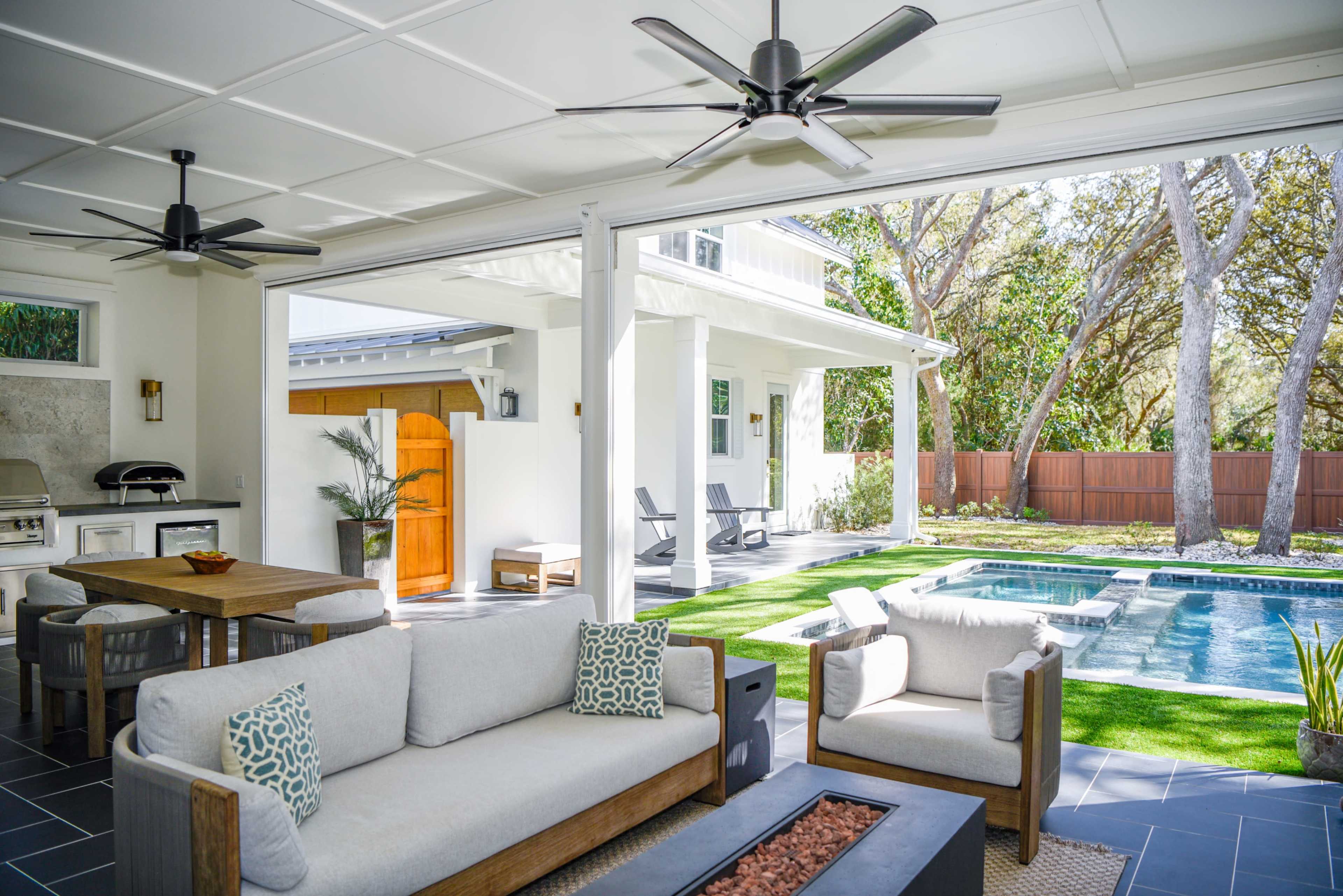 A spacious outdoor patio features comfortable seating arrangements, a dining area, and a swimming pool, surrounded by landscaped greenery.