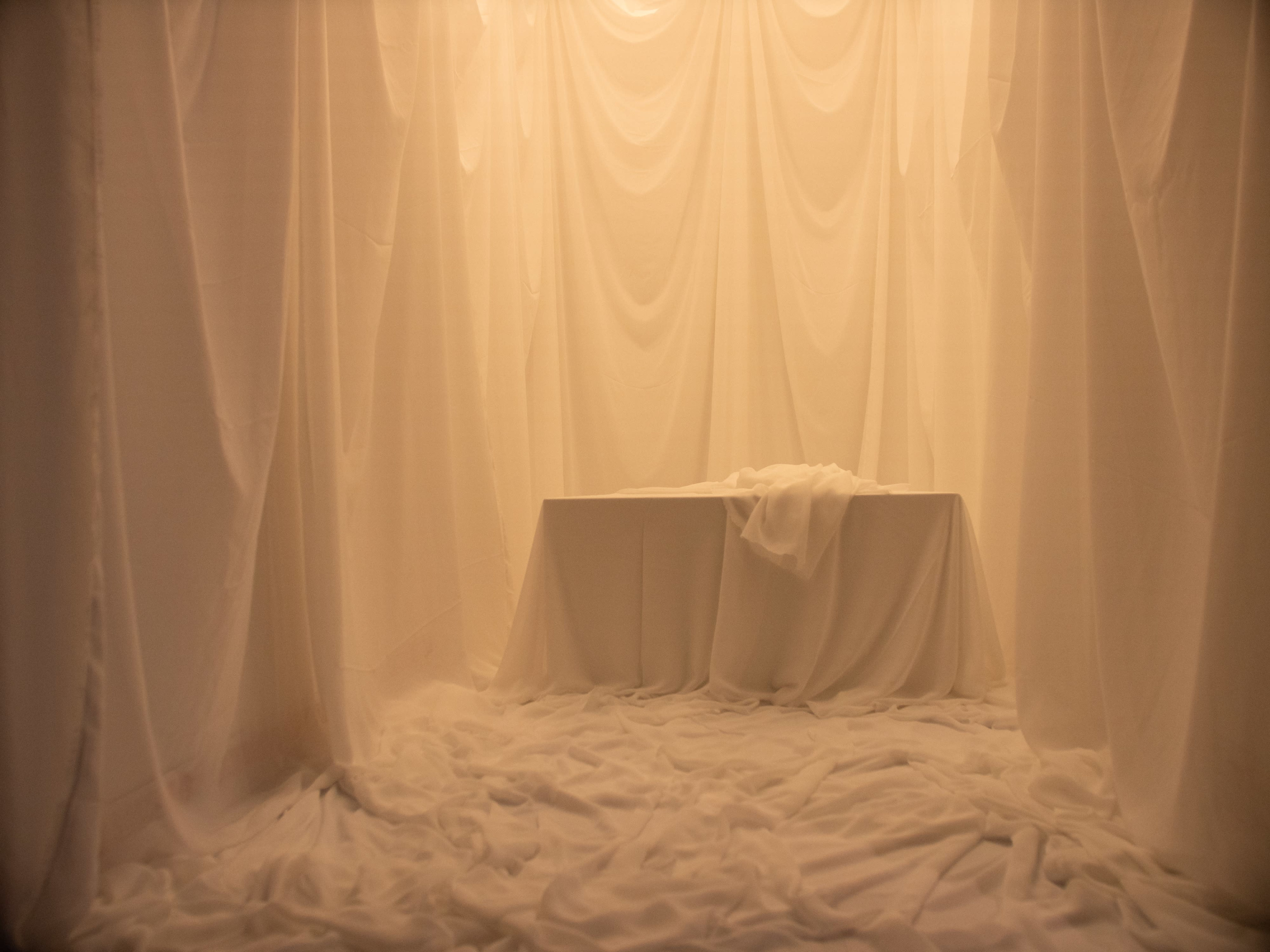 A room is completely draped in white fabric, featuring a table covered with a cloth in the center.