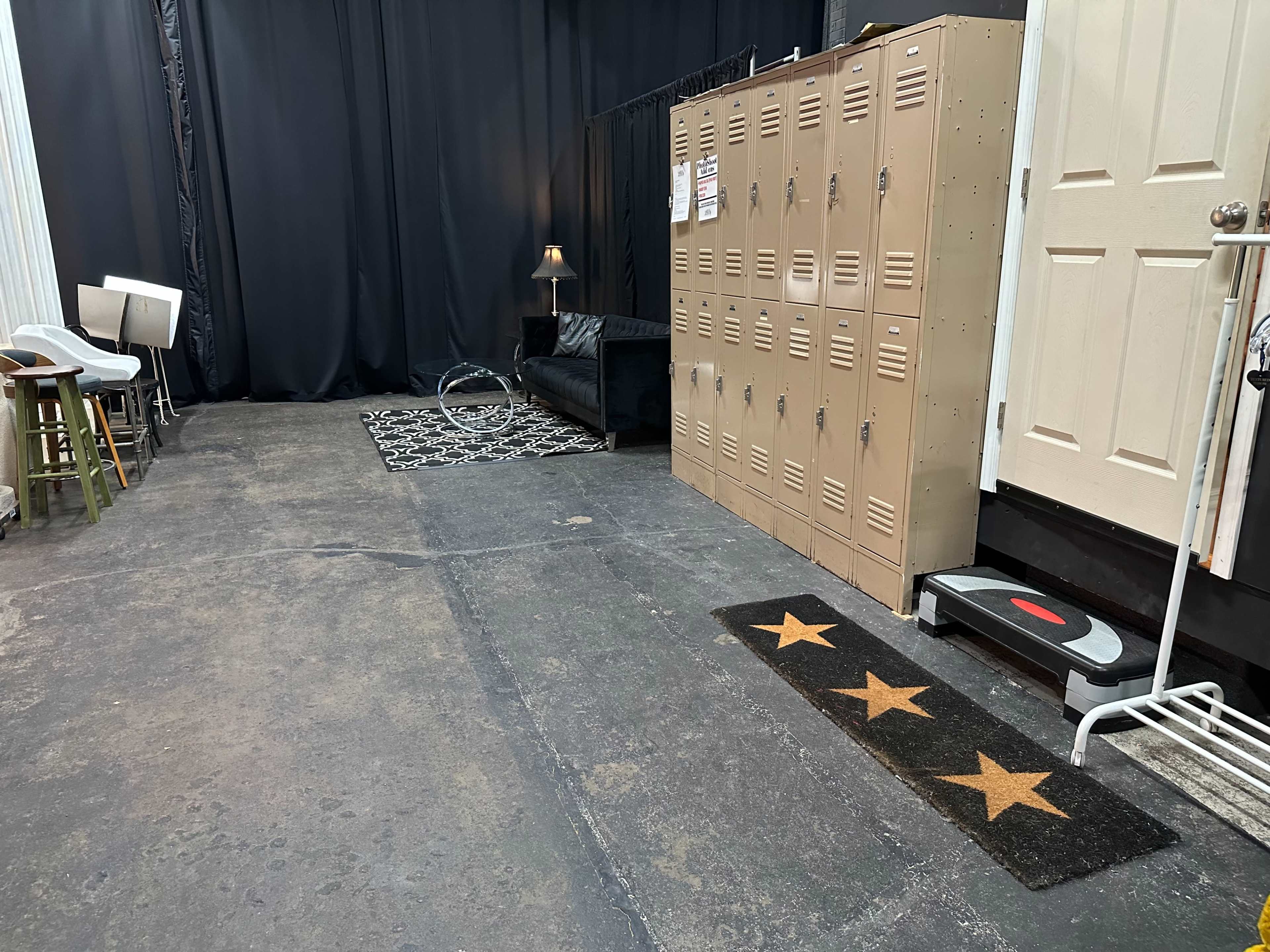 The image shows a dimly lit room featuring metal lockers along one wall, a black couch, and a rug with three stars on the floor.