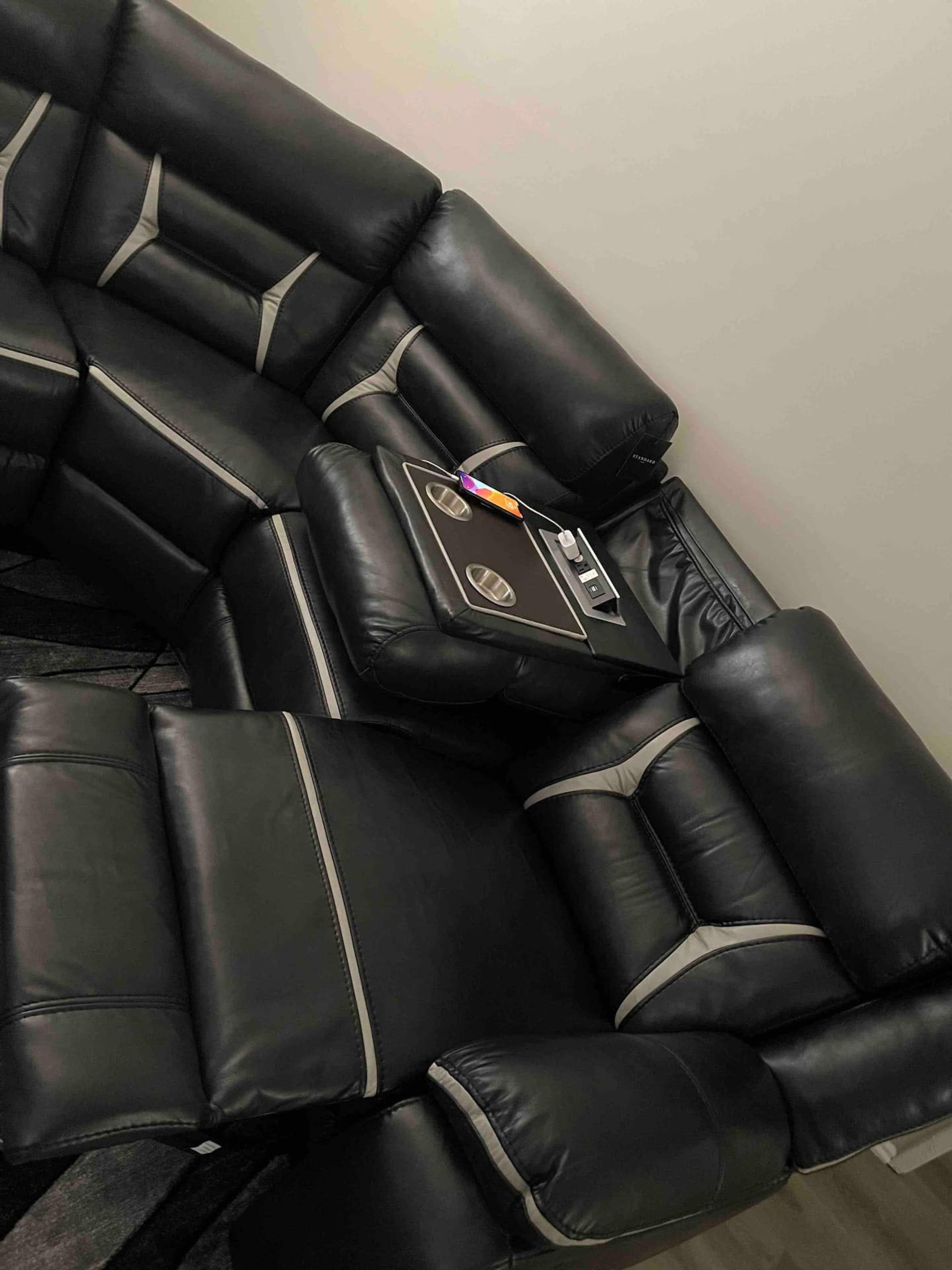 A black leather sectional sofa with a built-in storage compartment and small items placed on the center table.