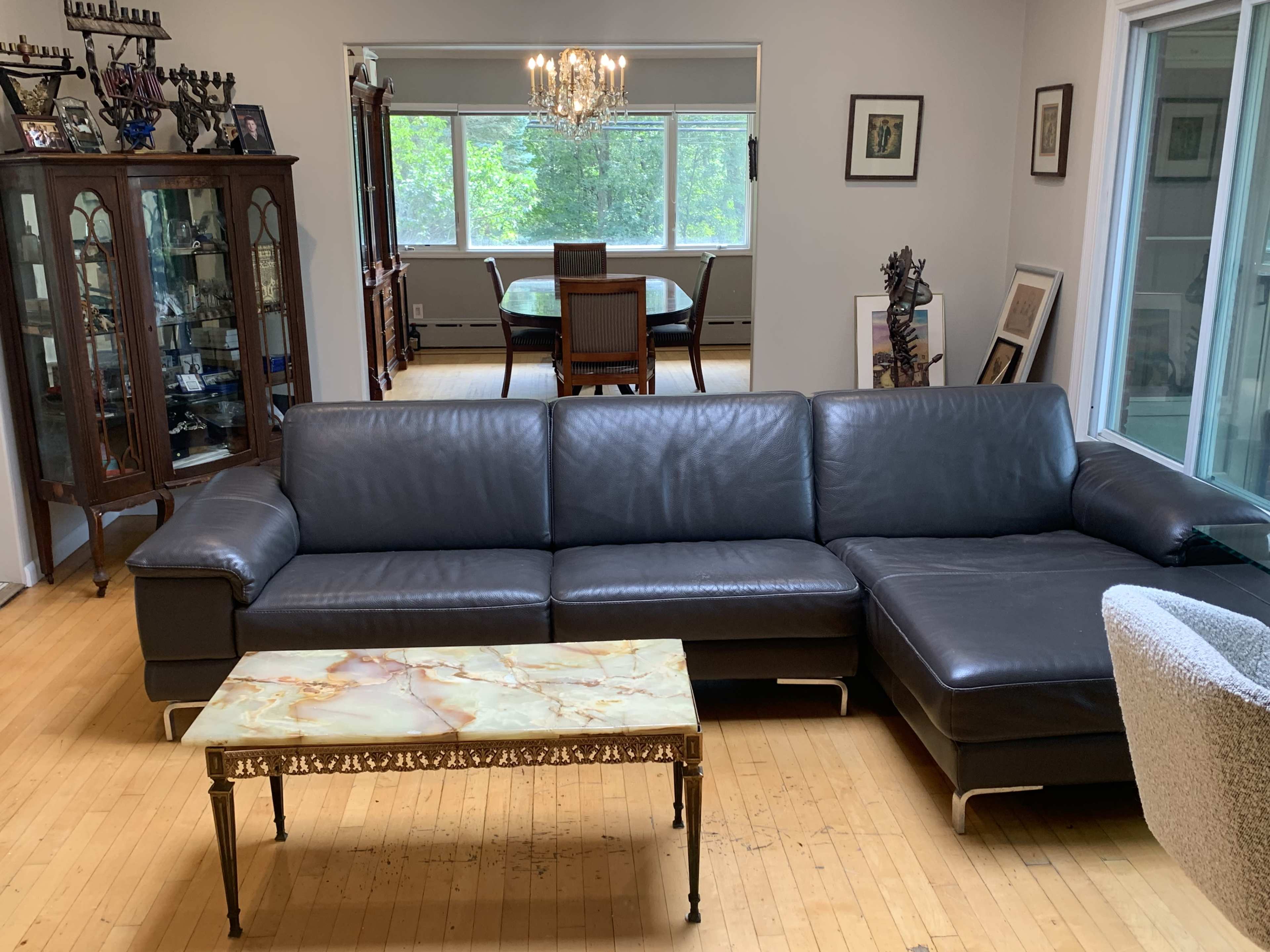 The scene features a living room with a dark leather sectional sofa, a marble-top coffee table, and a dining area visible in the background.
