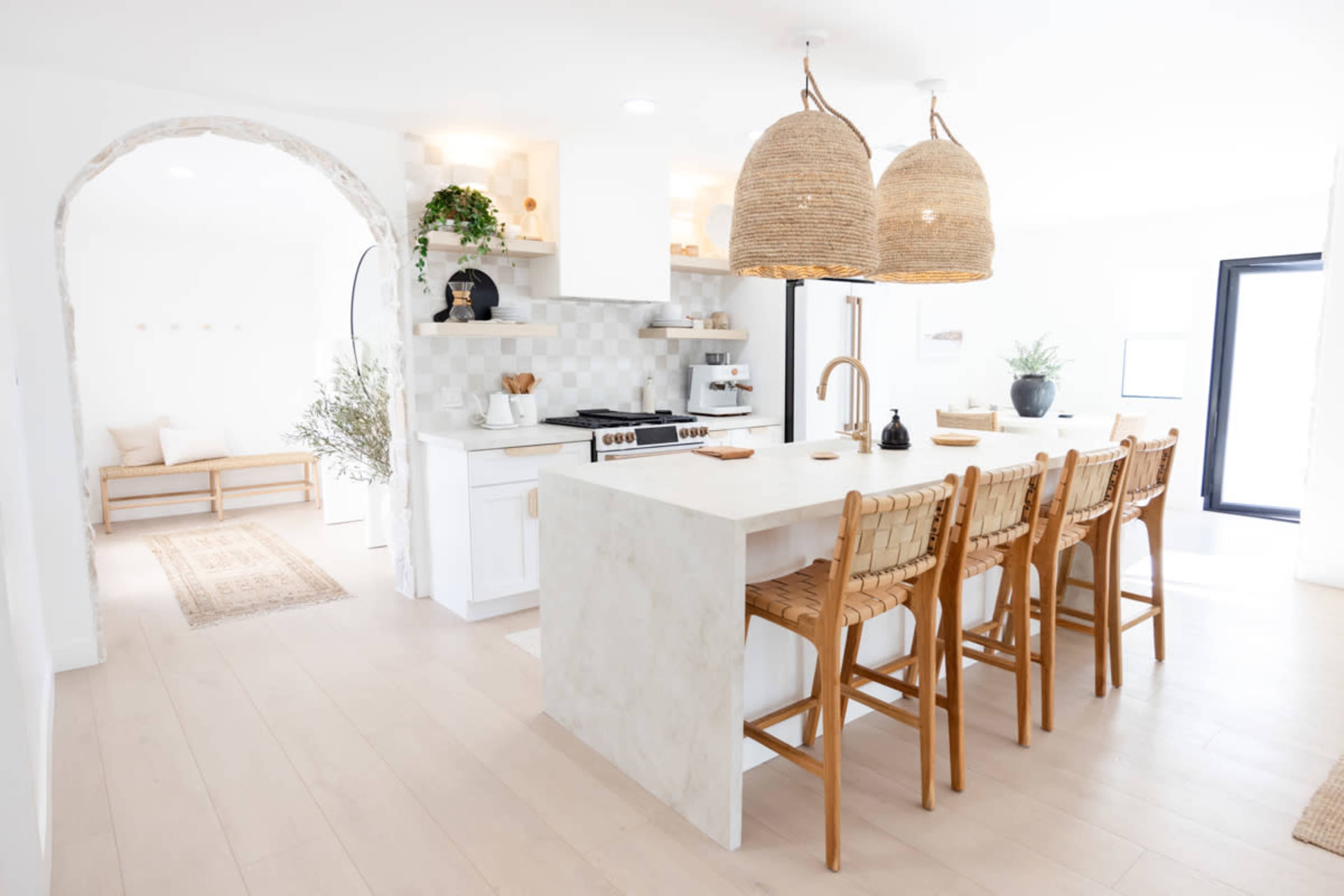 A modern kitchen features a large island with bar seating, white cabinetry, and two woven pendant lights.