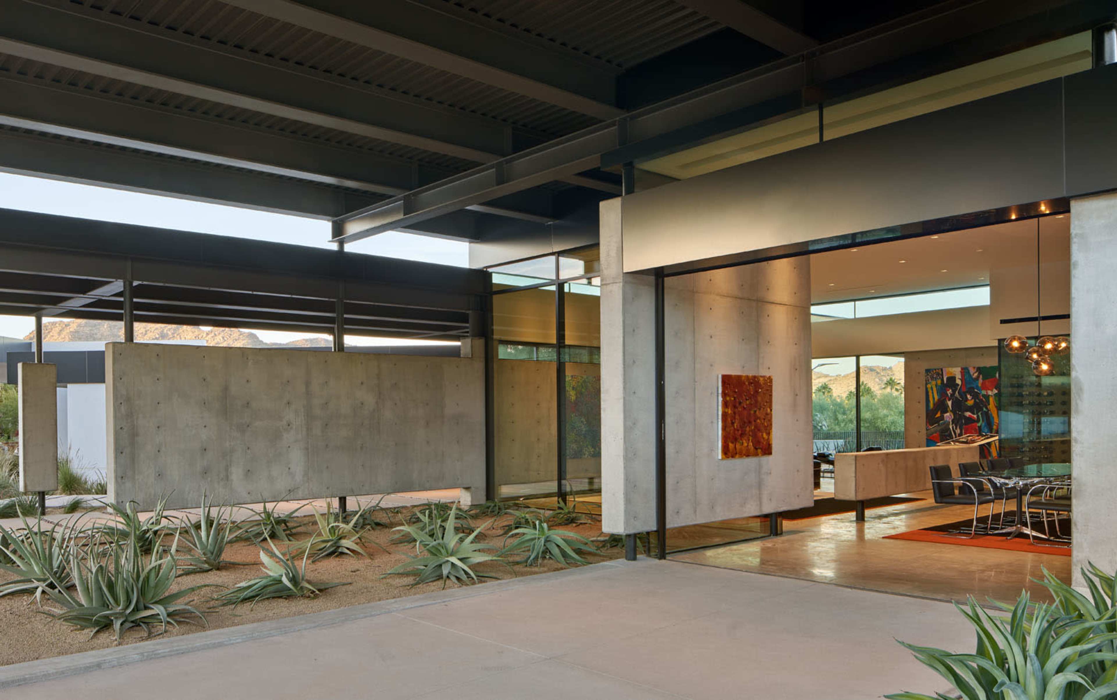A modern architectural structure featuring concrete walls and large glass windows, with a desert landscape visible through the entrance.