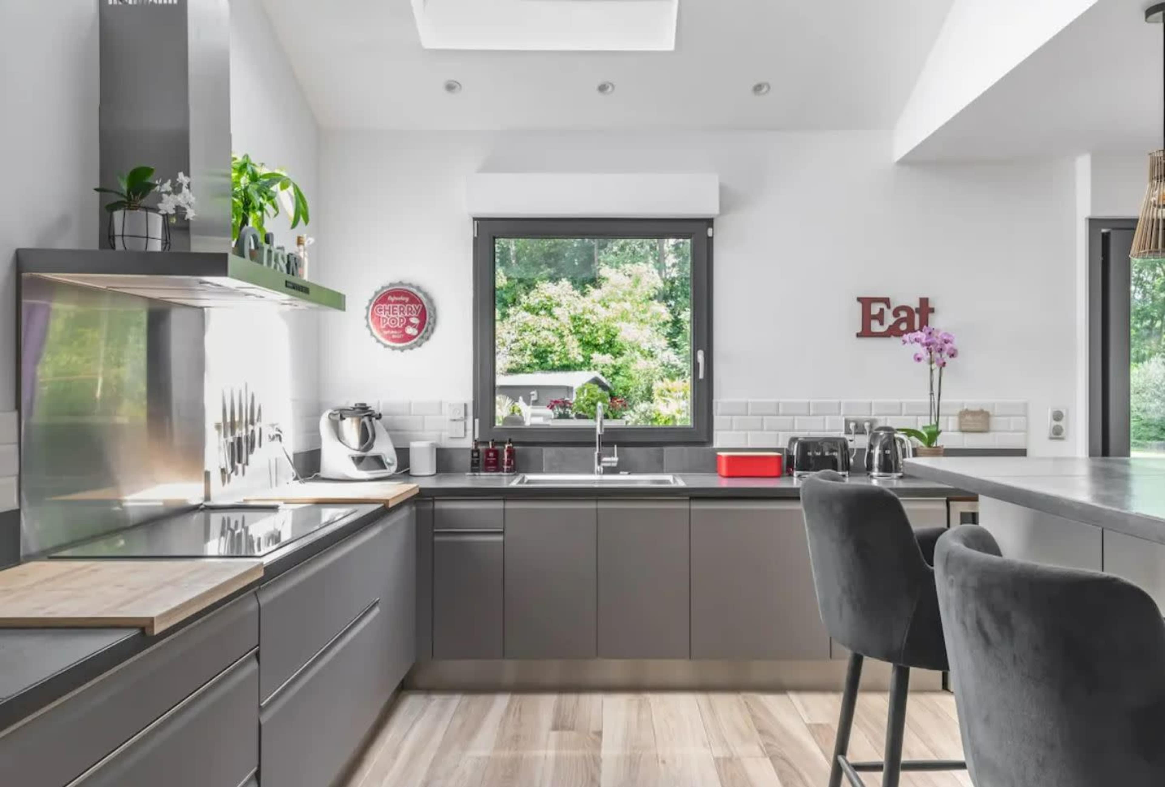 A modern kitchen with gray cabinets, a stainless steel sink, and a breakfast bar with gray stools.