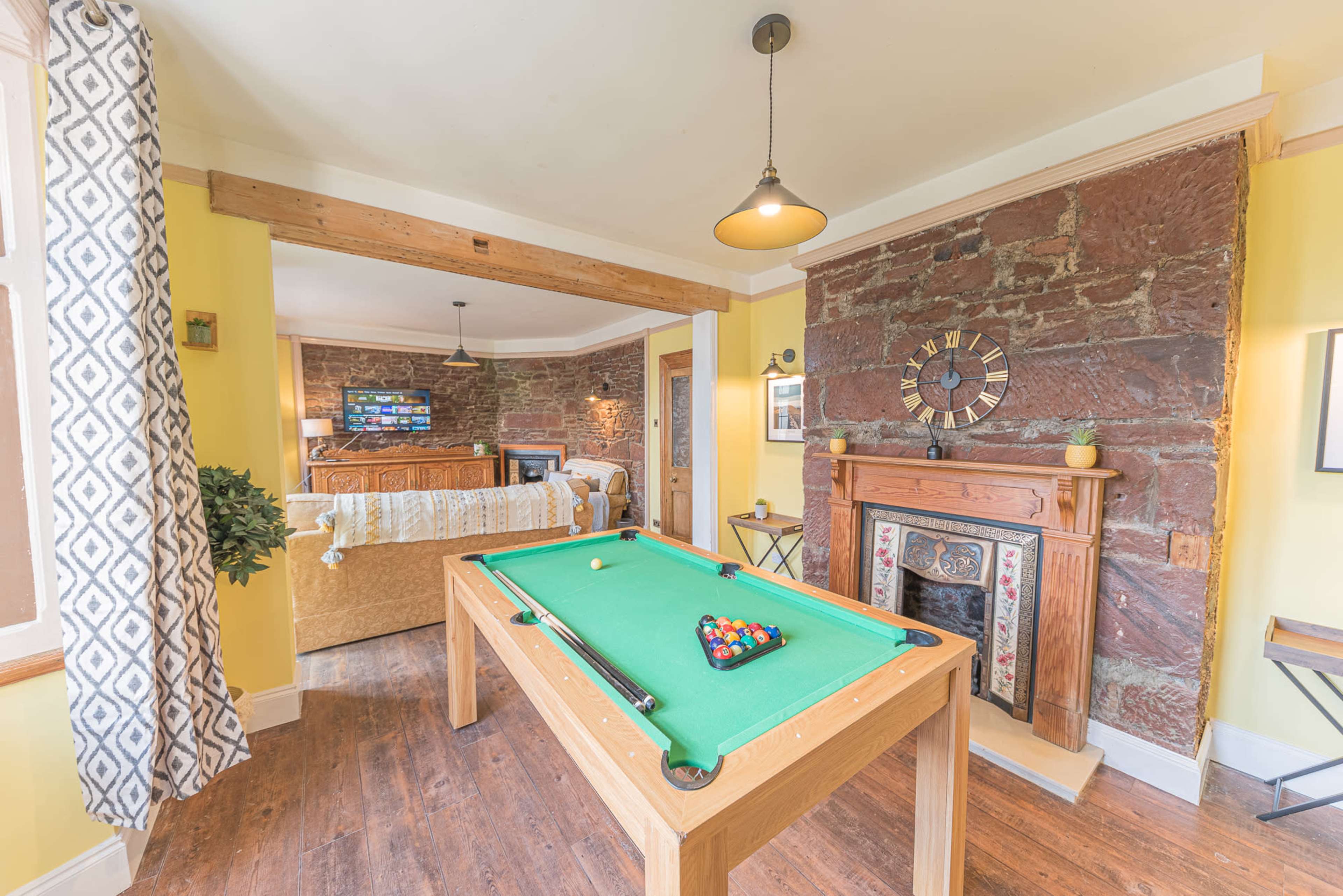 A room featuring a pool table, a cozy sitting area with a television, and a decorative fireplace surrounded by stone walls.