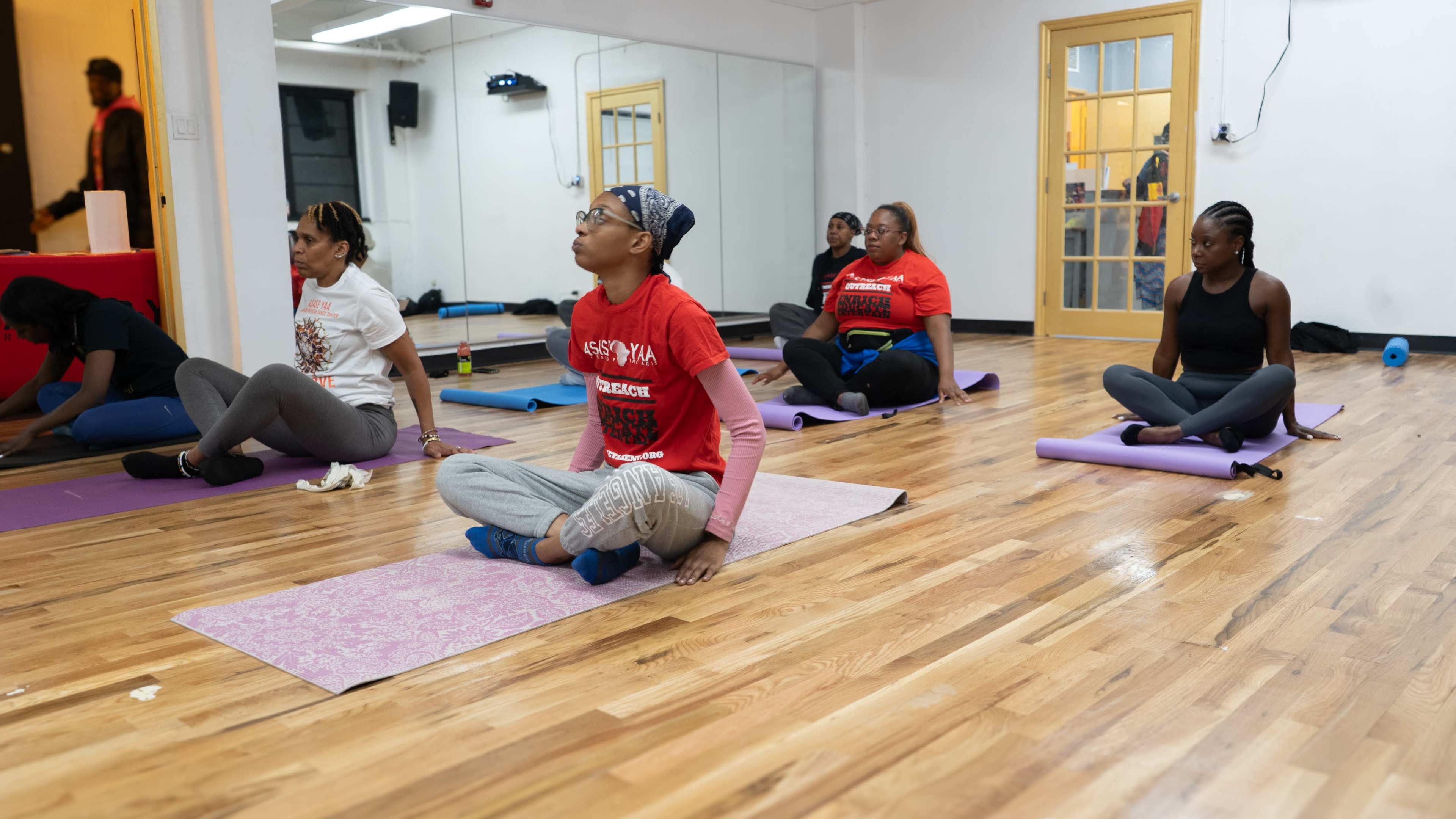 A group of women are practicing yoga in a bright, spacious studio with wooden floors and mirrors.
