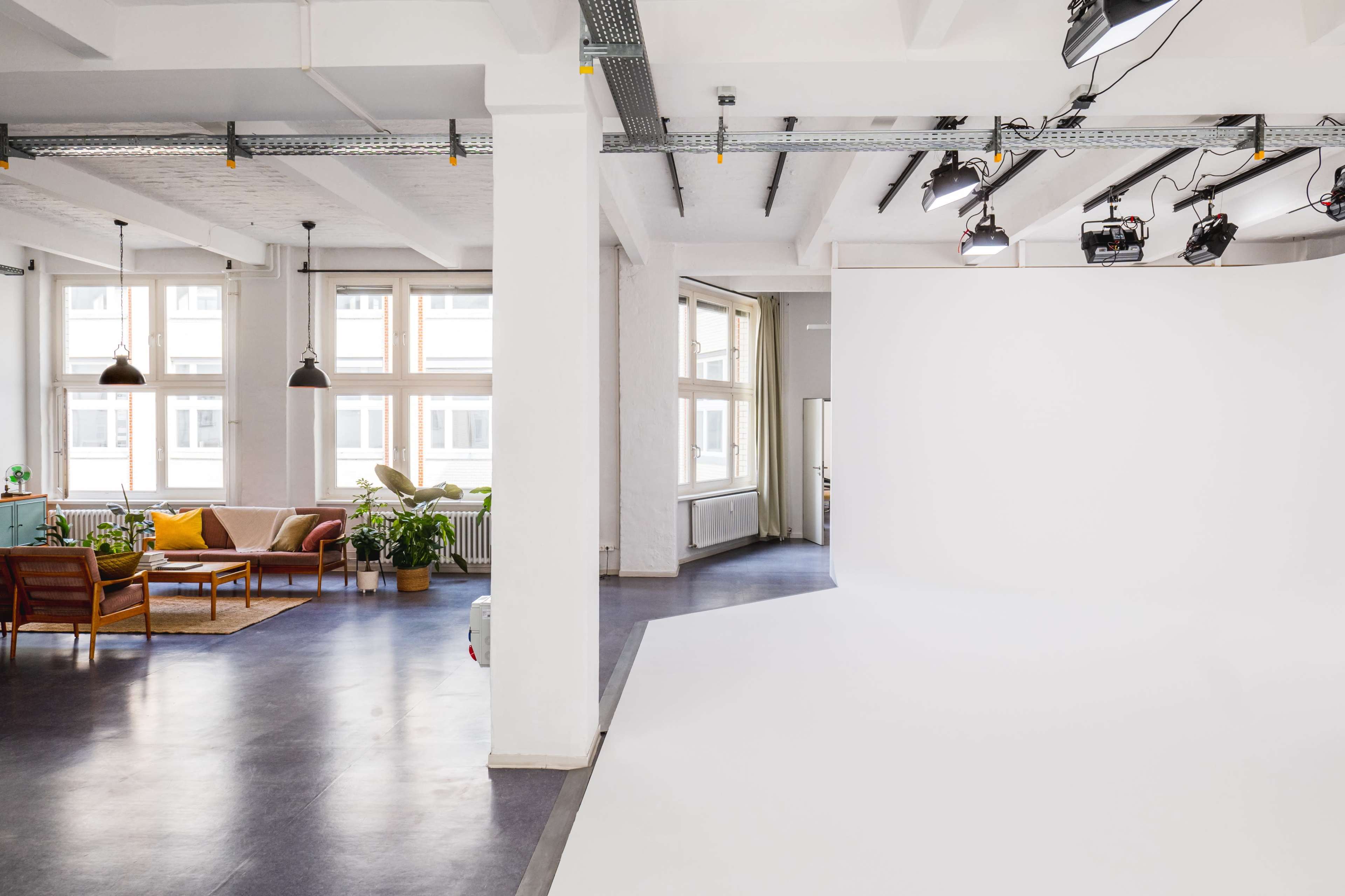 A spacious, modern studio with large windows, a seating area, and a white backdrop on one side.