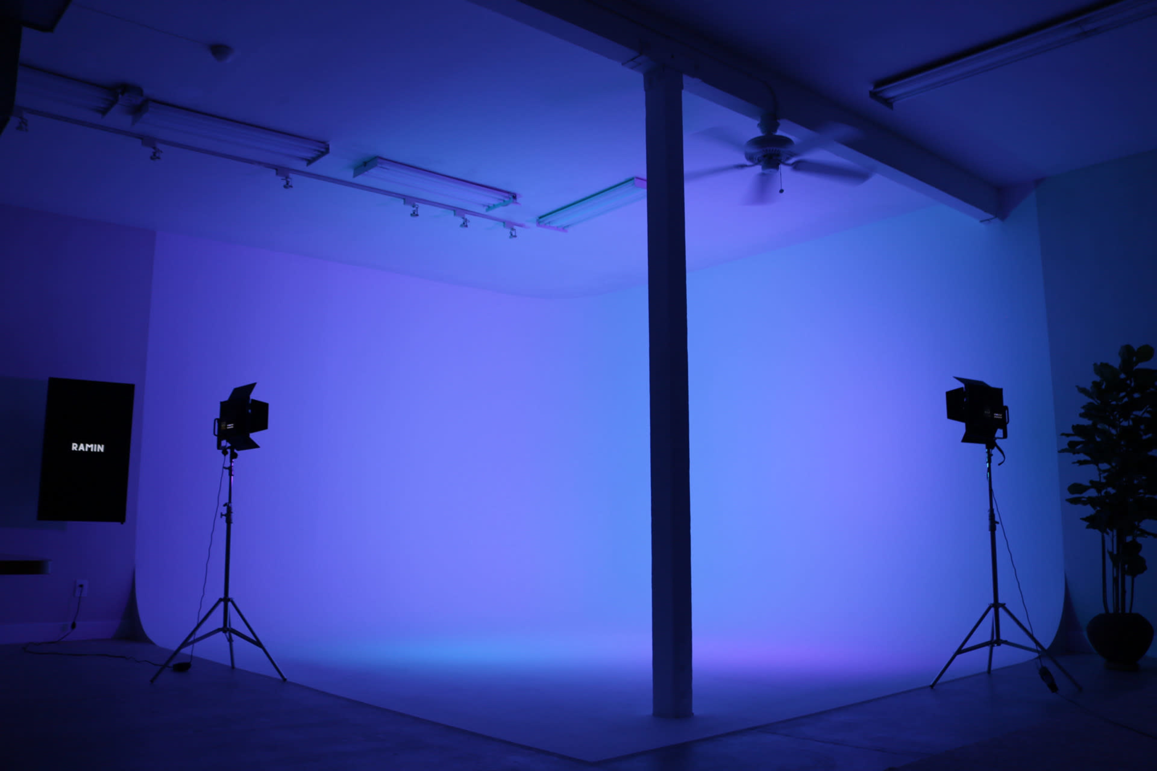 A brightly lit photography studio features two studio lights on tripods and a large, plain backdrop illuminated in shades of blue and purple.