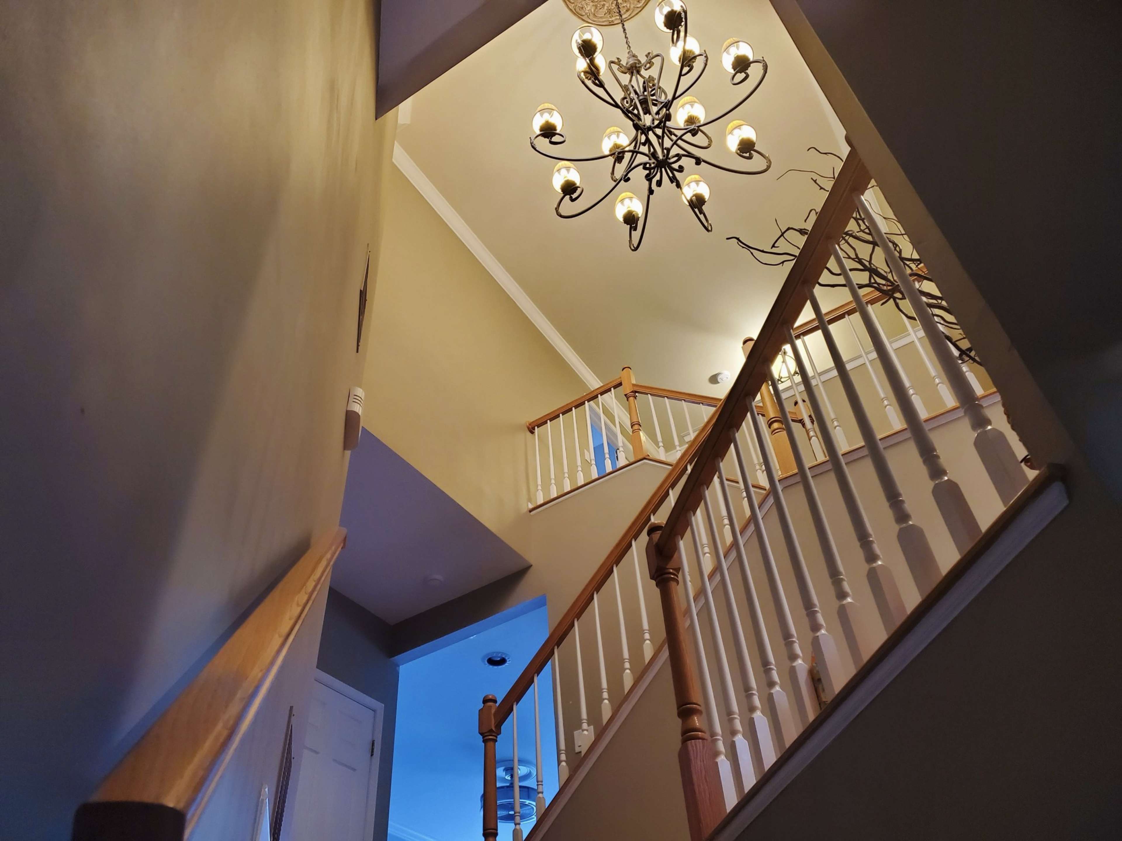 A staircase with wooden railings leading to an upper landing, illuminated by a chandelier.