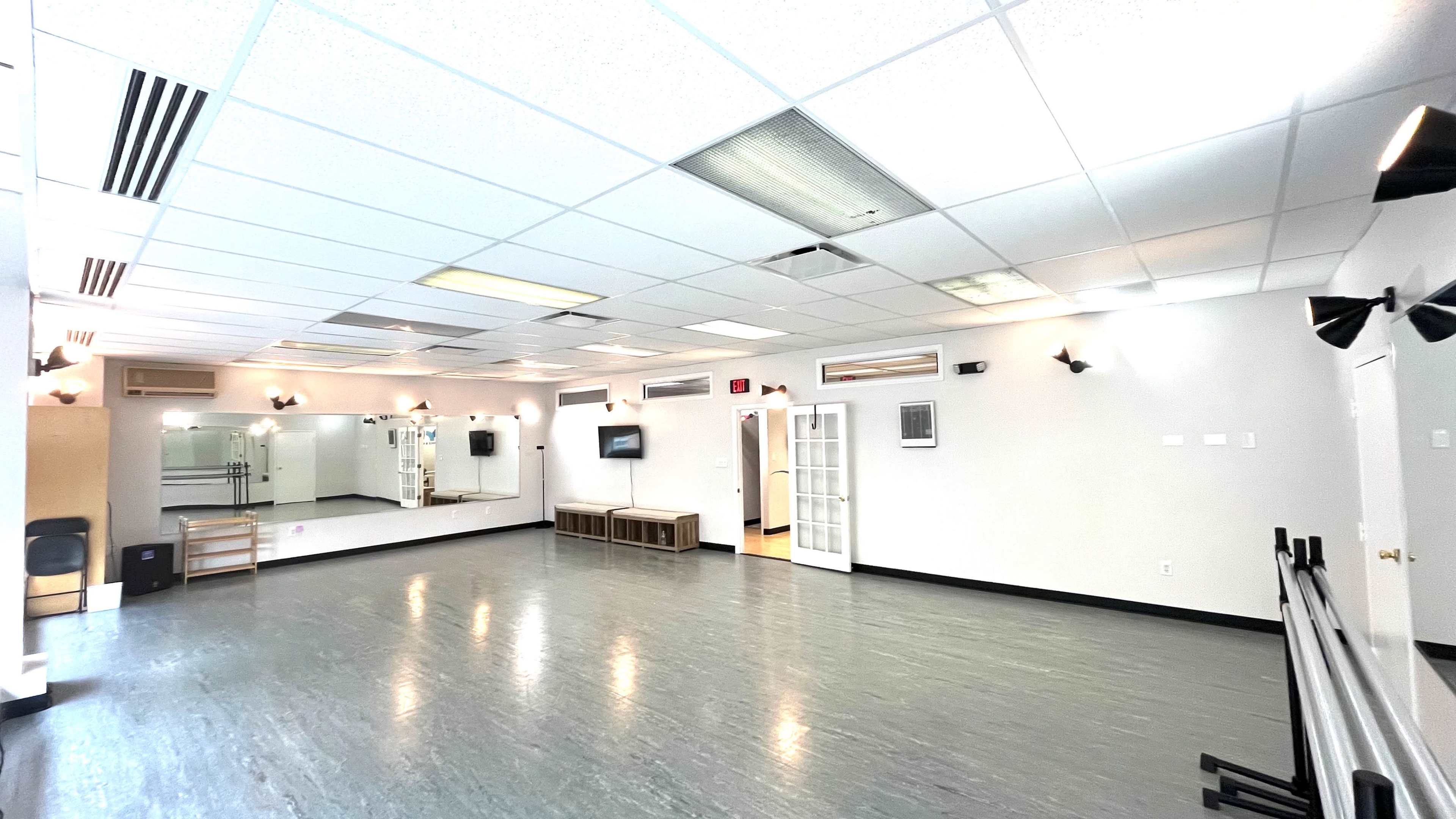 A spacious dance studio features mirrored walls, wooden furniture, and various lighting fixtures.