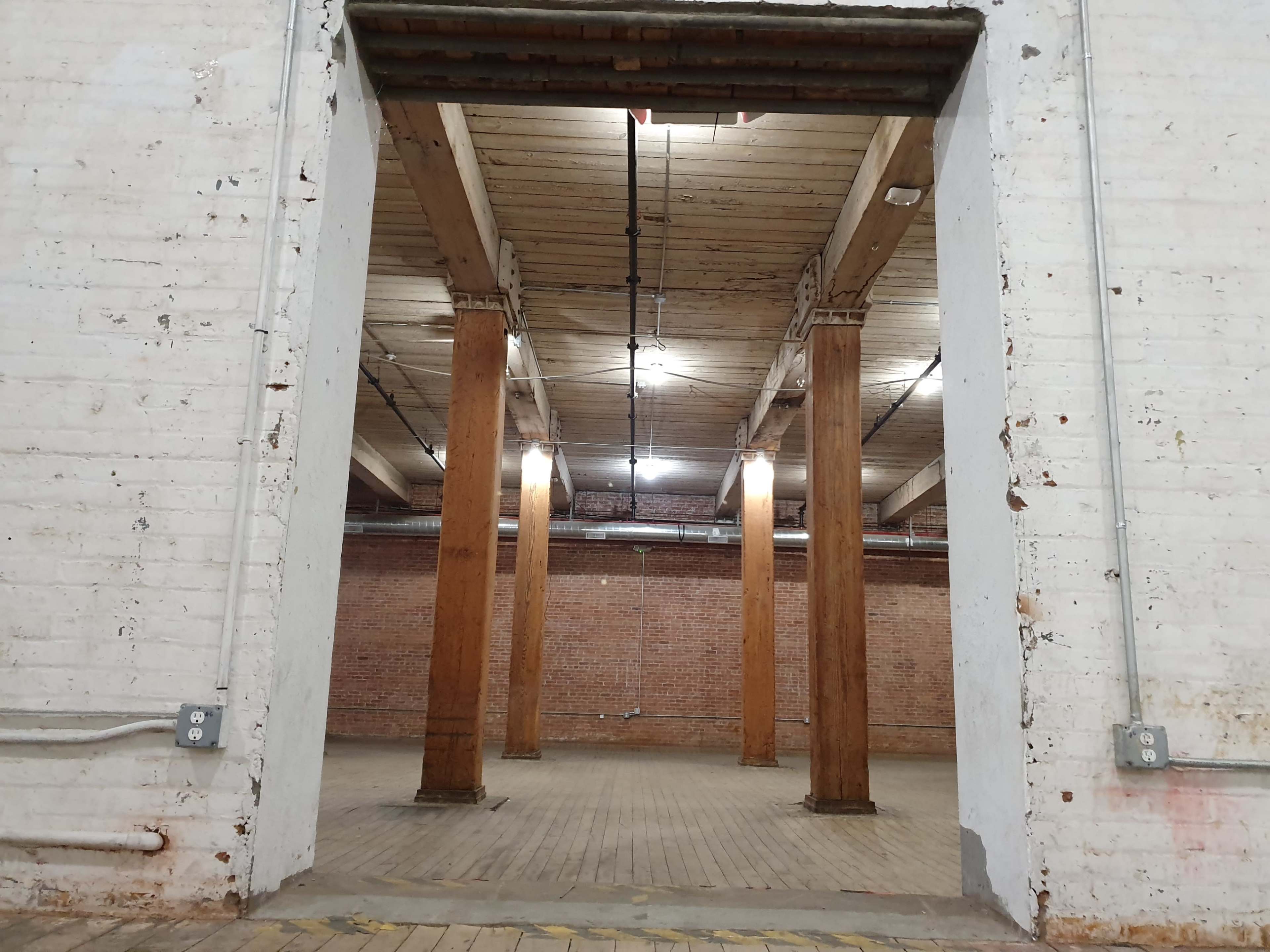 A large, empty room with wooden pillars and exposed brick walls, illuminated by overhead lights.