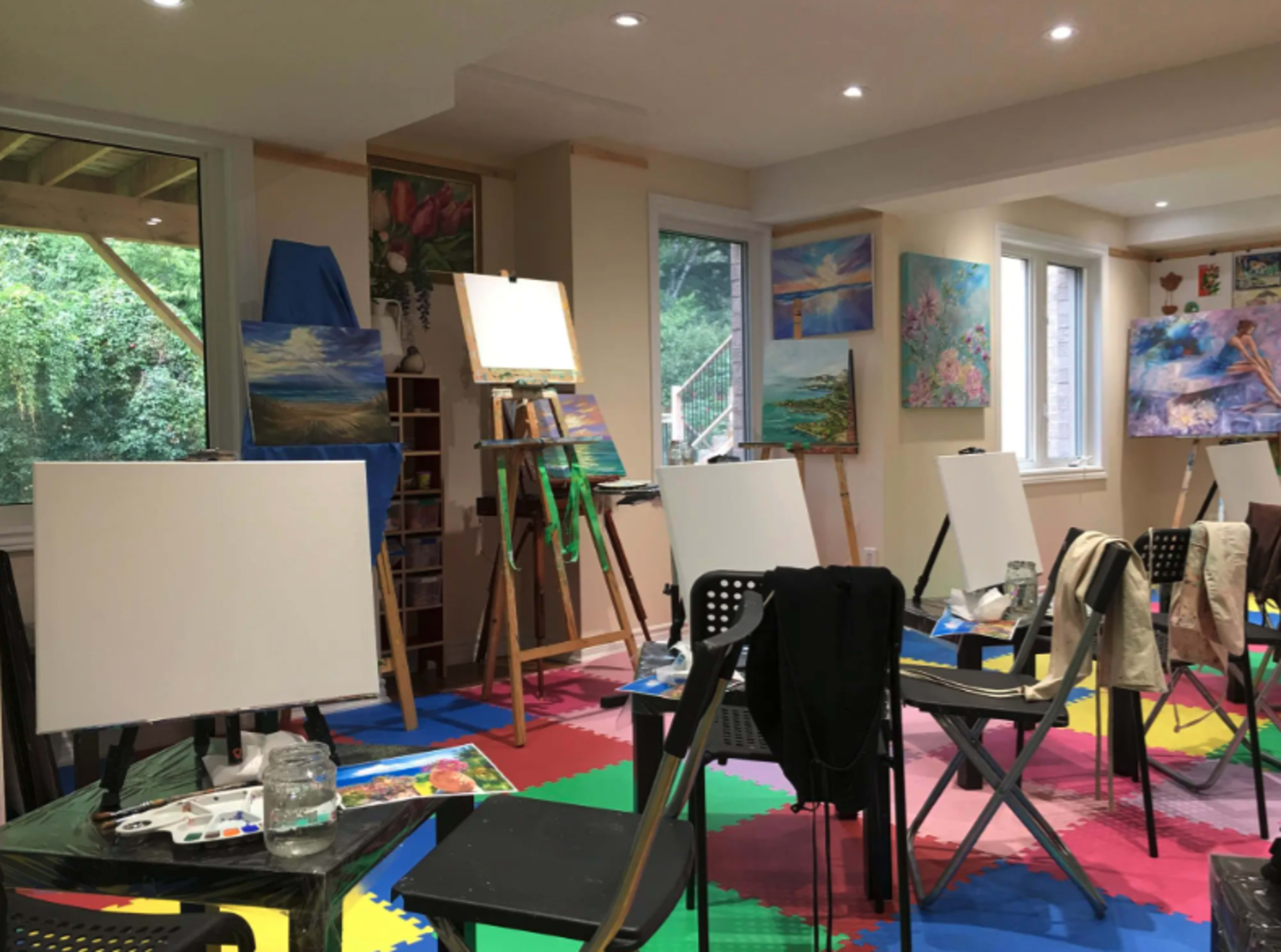 An art studio with empty canvases on easels, scattered art supplies on tables, and colorful artwork displayed on the walls.
