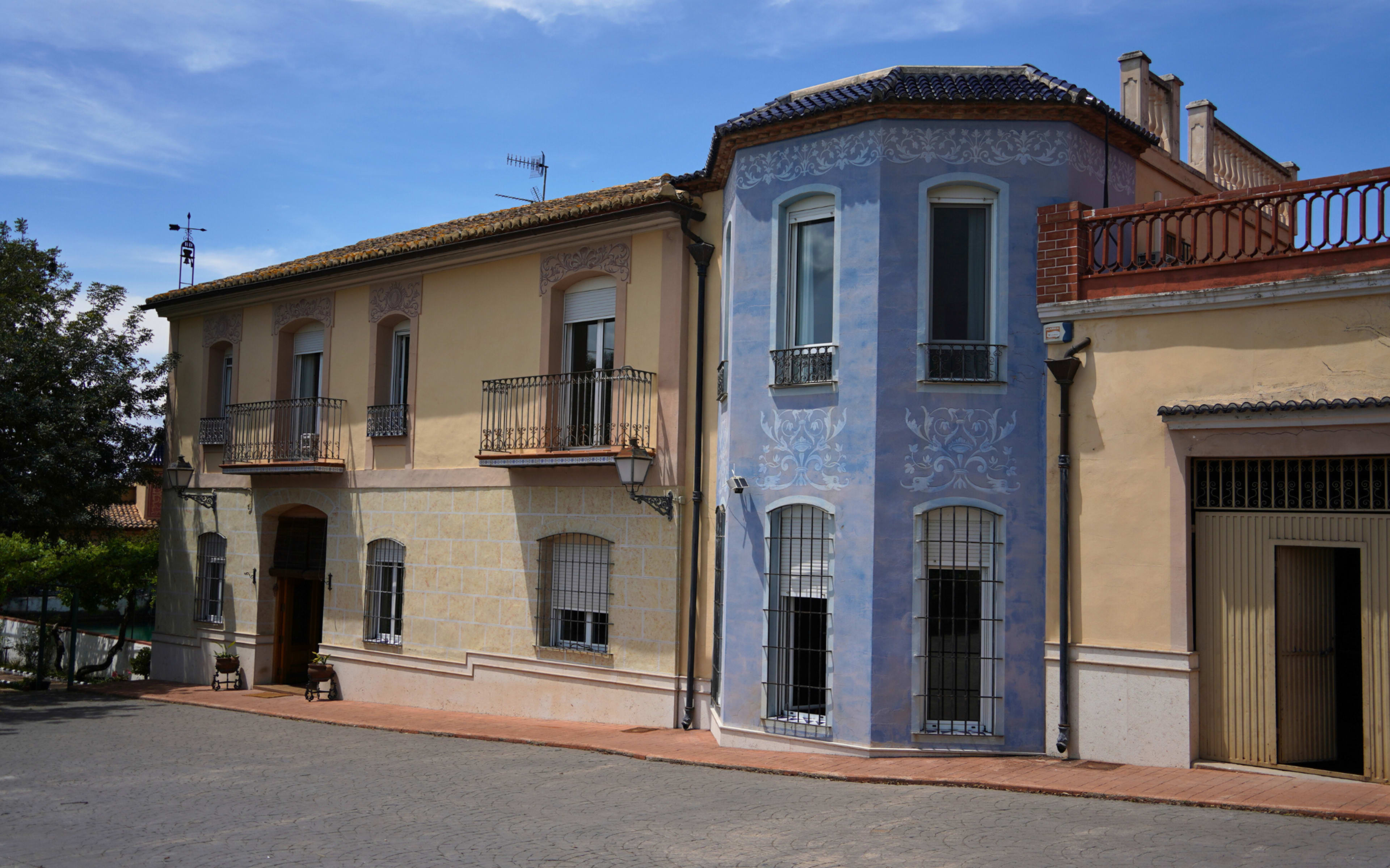 The image shows a colorful residential building with a painted blue corner and decorative elements, situated on a cobblestone street.