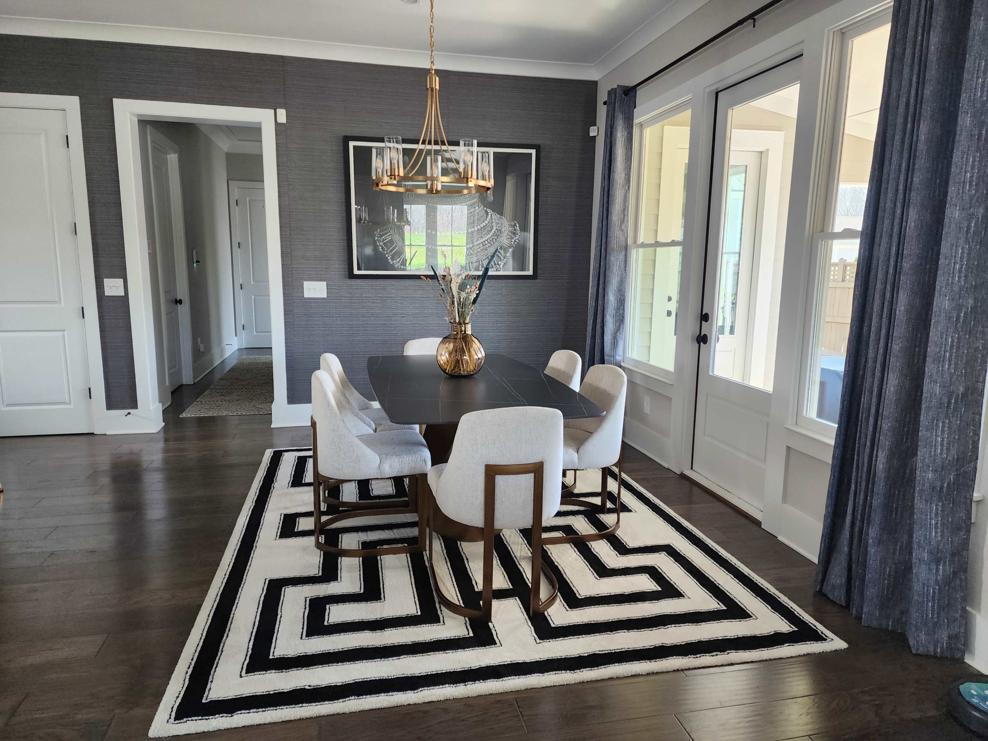 A dining area features a round table surrounded by four upholstered chairs on a geometric rug, with a pendant light hanging above.