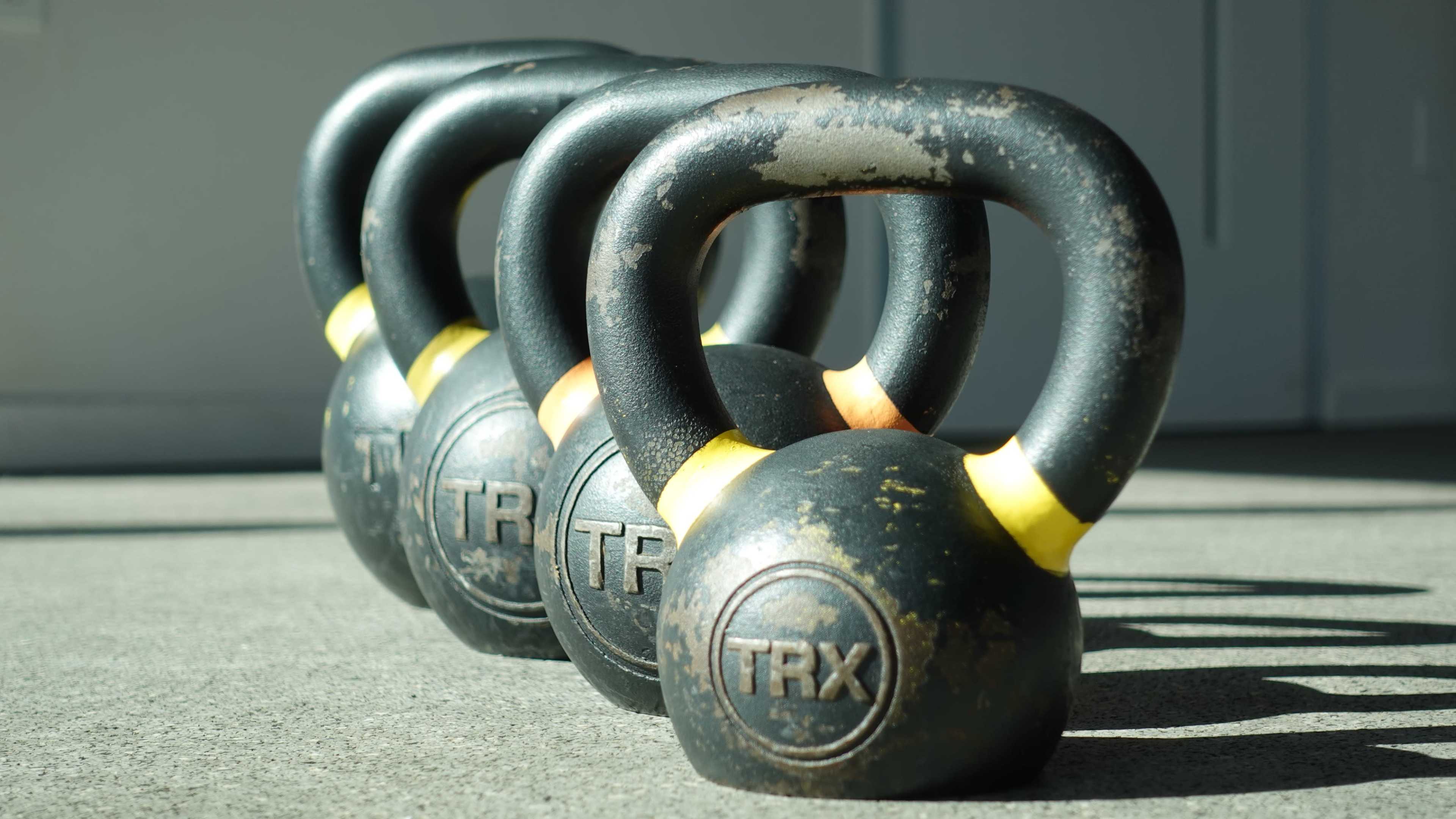A row of four kettlebells with yellow accents sits on a concrete floor.