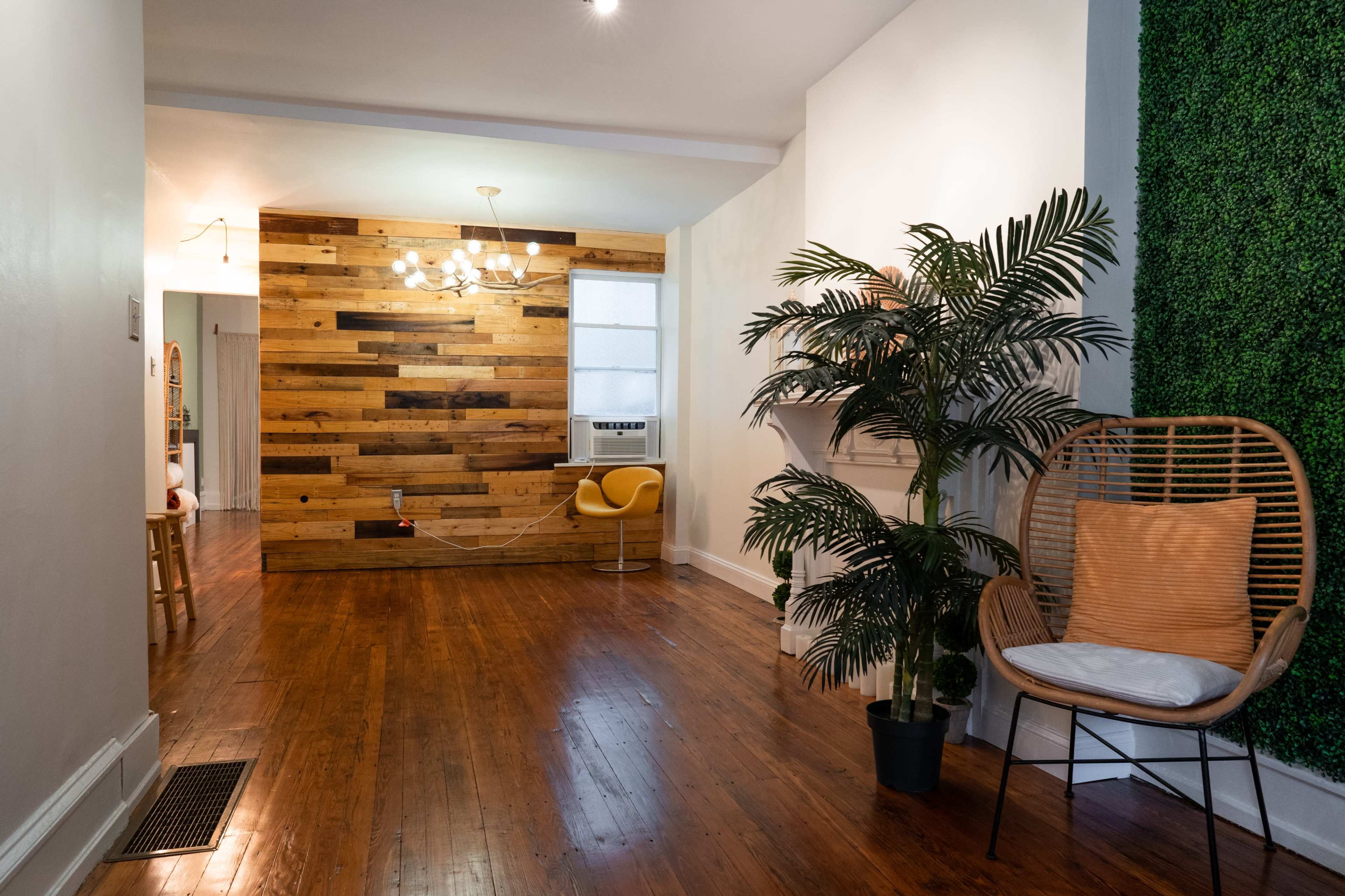 A hallway leading to a room with a wooden accent wall, a modern light fixture, and decorative greenery.