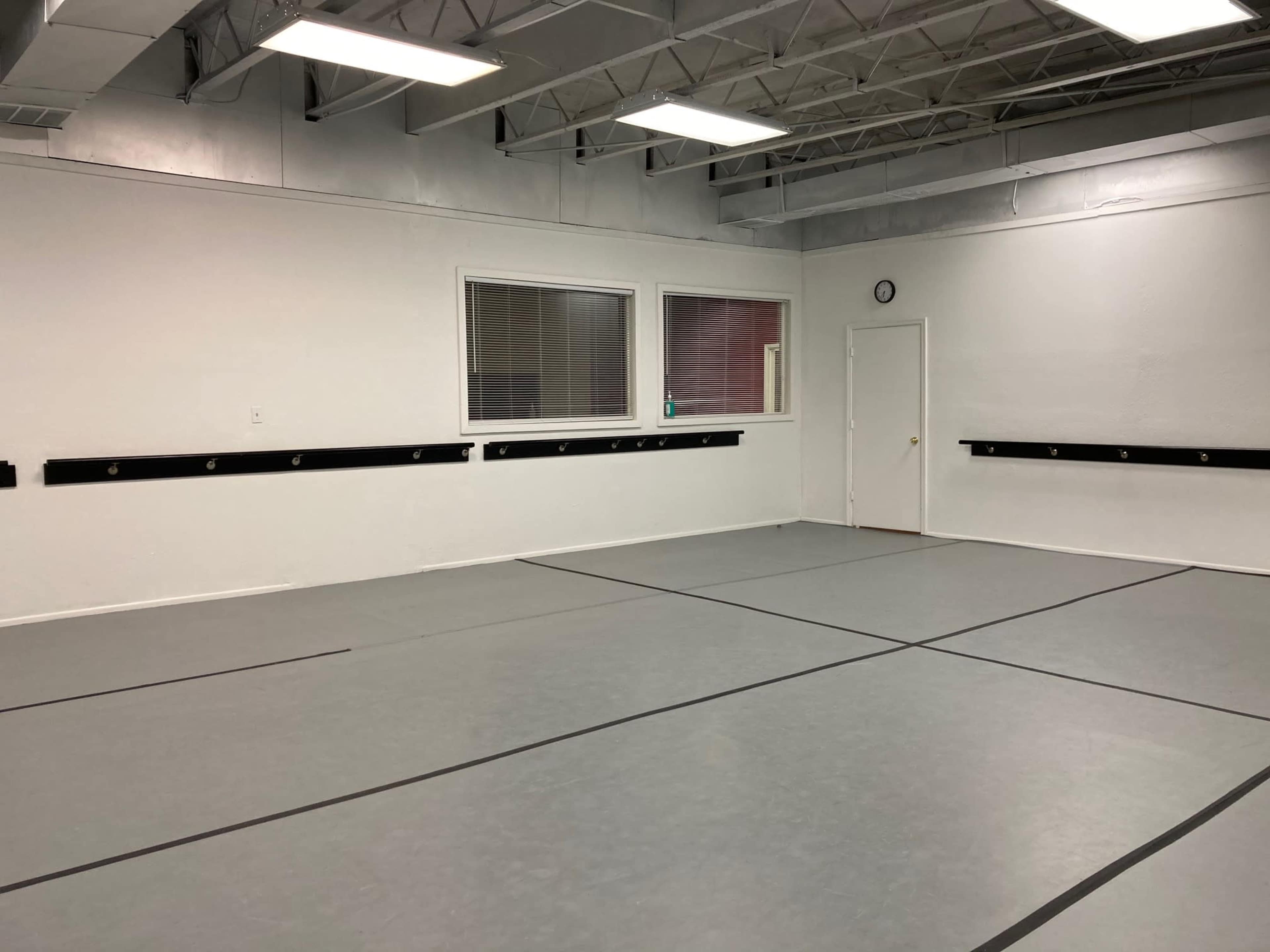 A spacious room with a gray floor, white walls, a clock on one wall, and several hooks mounted along another wall.