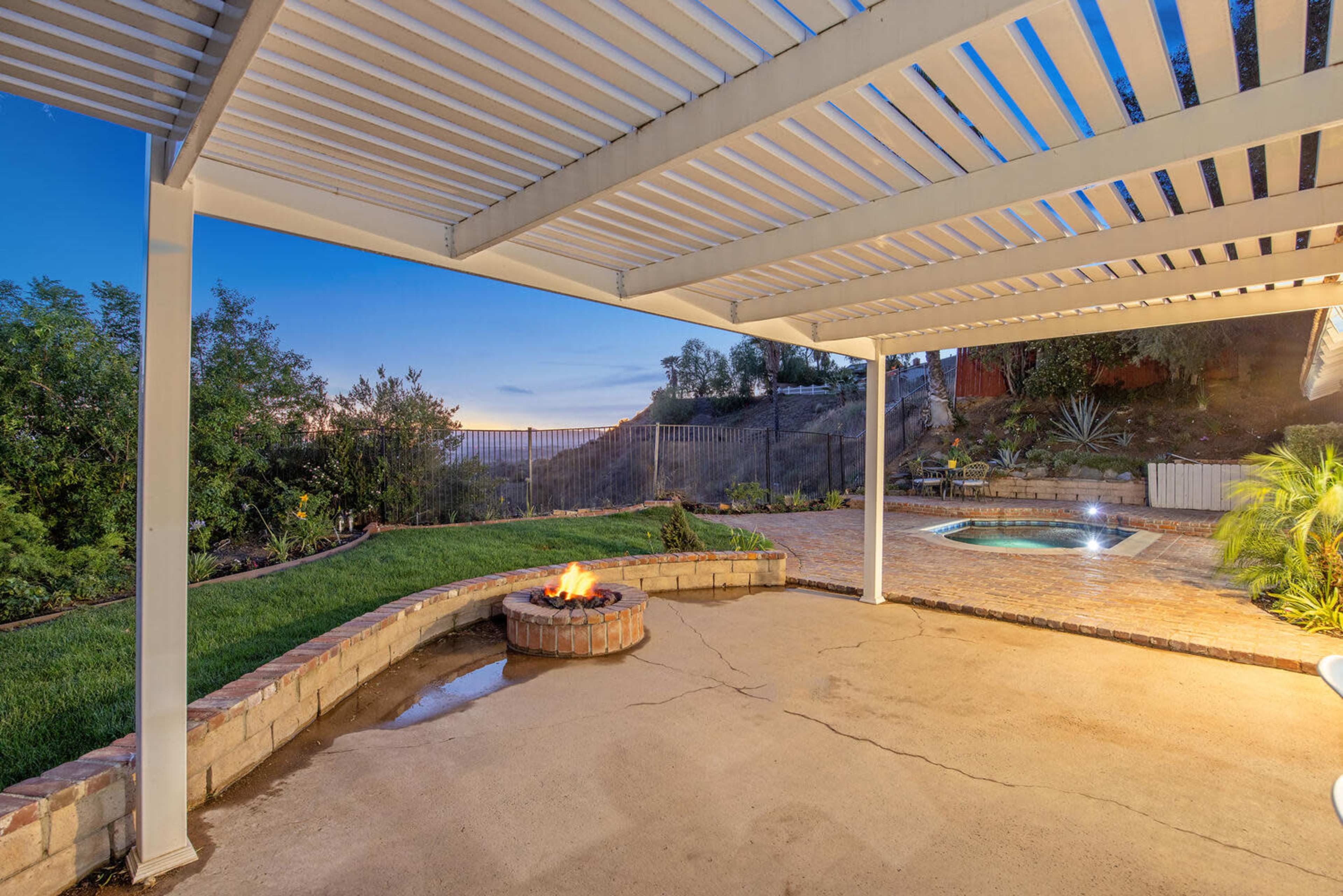 A patio area with a fire pit and a swimming pool overlooks a landscaped yard and a scenic view.